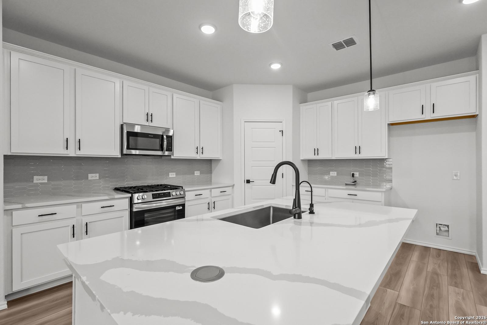 Modern white kitchen with quartz island, stainless appliances, subway tile backsplash in Davidson Homes The Douglas E, San Antonio