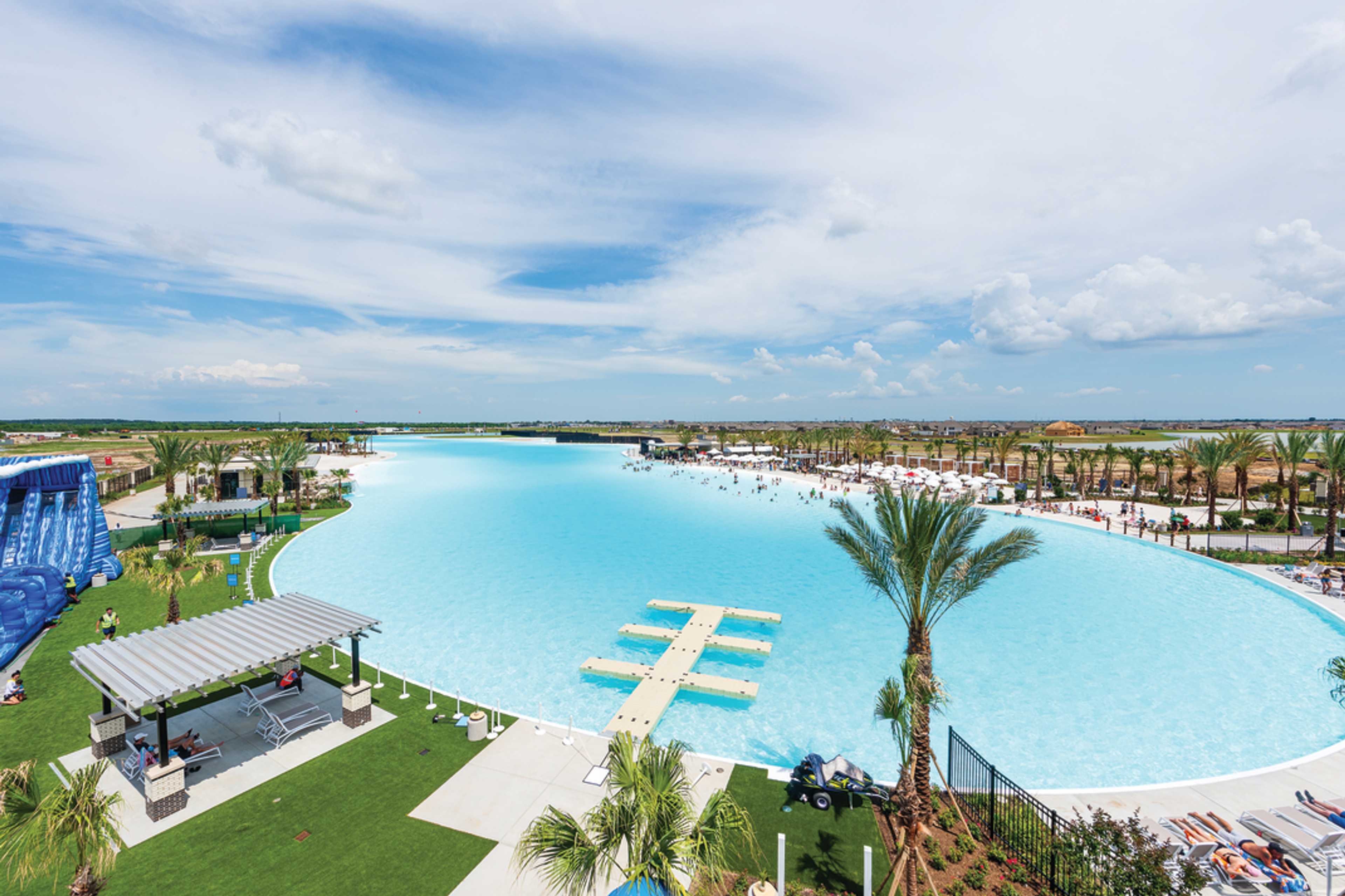 Resort-style lagoon pool at Lago Mar in Texas City TX with turquoise waters, palm trees, umbrellas, and shaded lounges