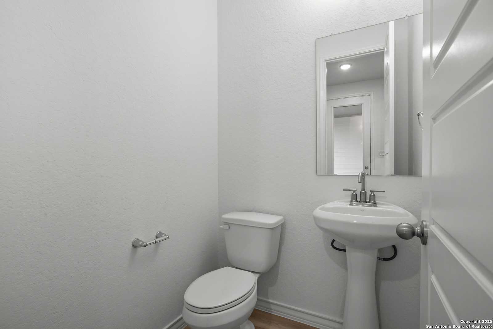 Bright white powder room with pedestal sink, toilet, and mirrored cabinet in The Summerlin B, Castroville, Texas