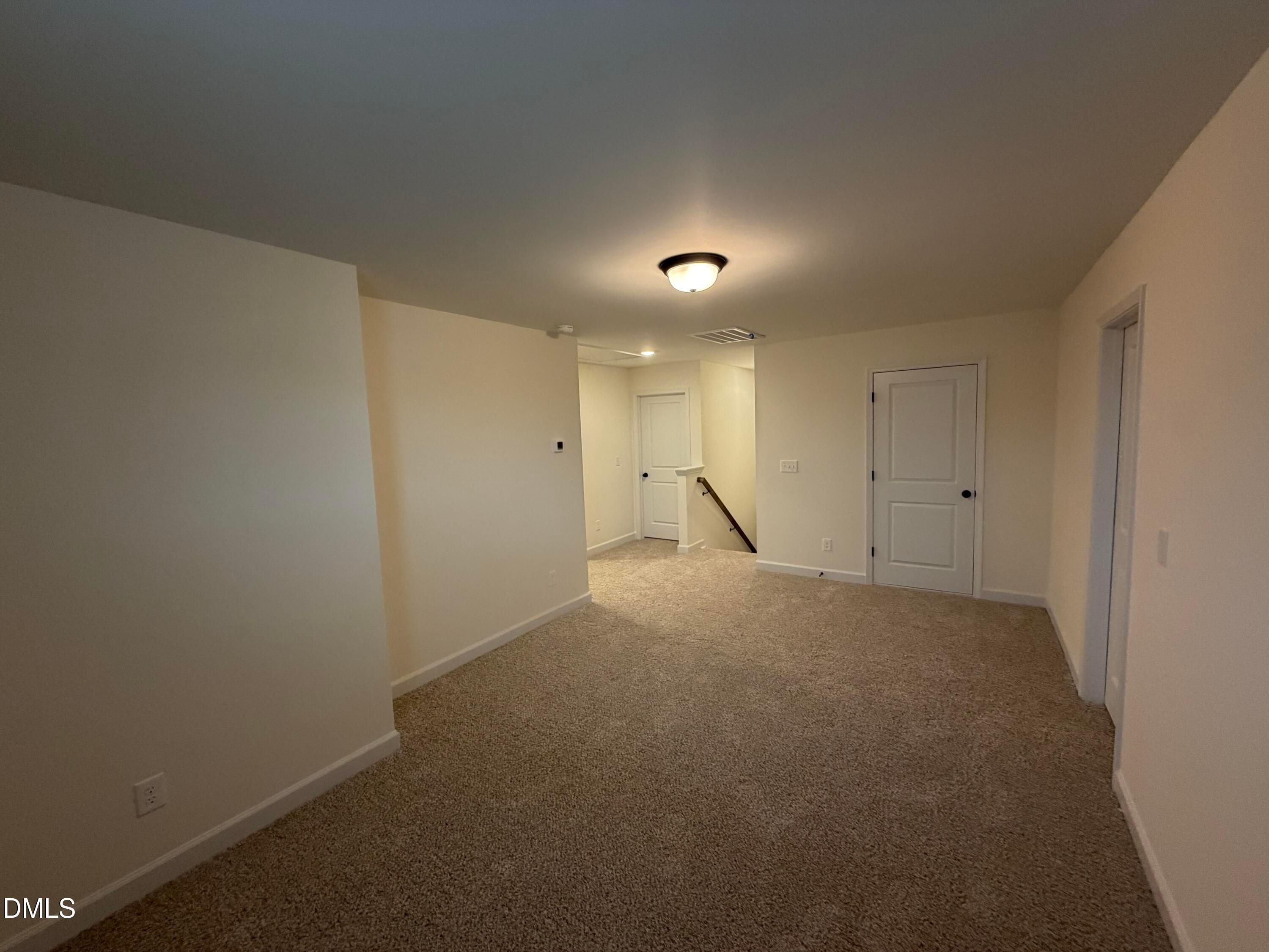 Spacious carpeted loft area with white doors and staircase in 2-story Ashport M home by Davidson Homes in Wendell, NC