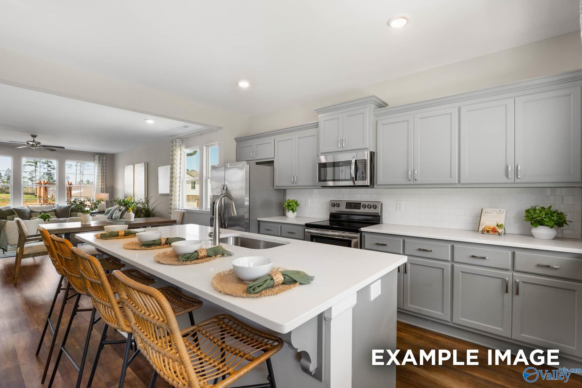 Modern open-concept kitchen with gray cabinets, quartz counters, stainless appliances, and rattan island stools in Davidson Homes The Stella, Madison, AL