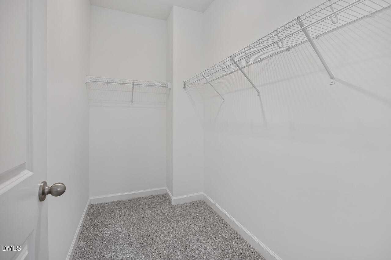 Spacious walk-in closet with wire shelving, white walls, and carpeted floor in Davidson Homes The Carter C, Lillington, NC