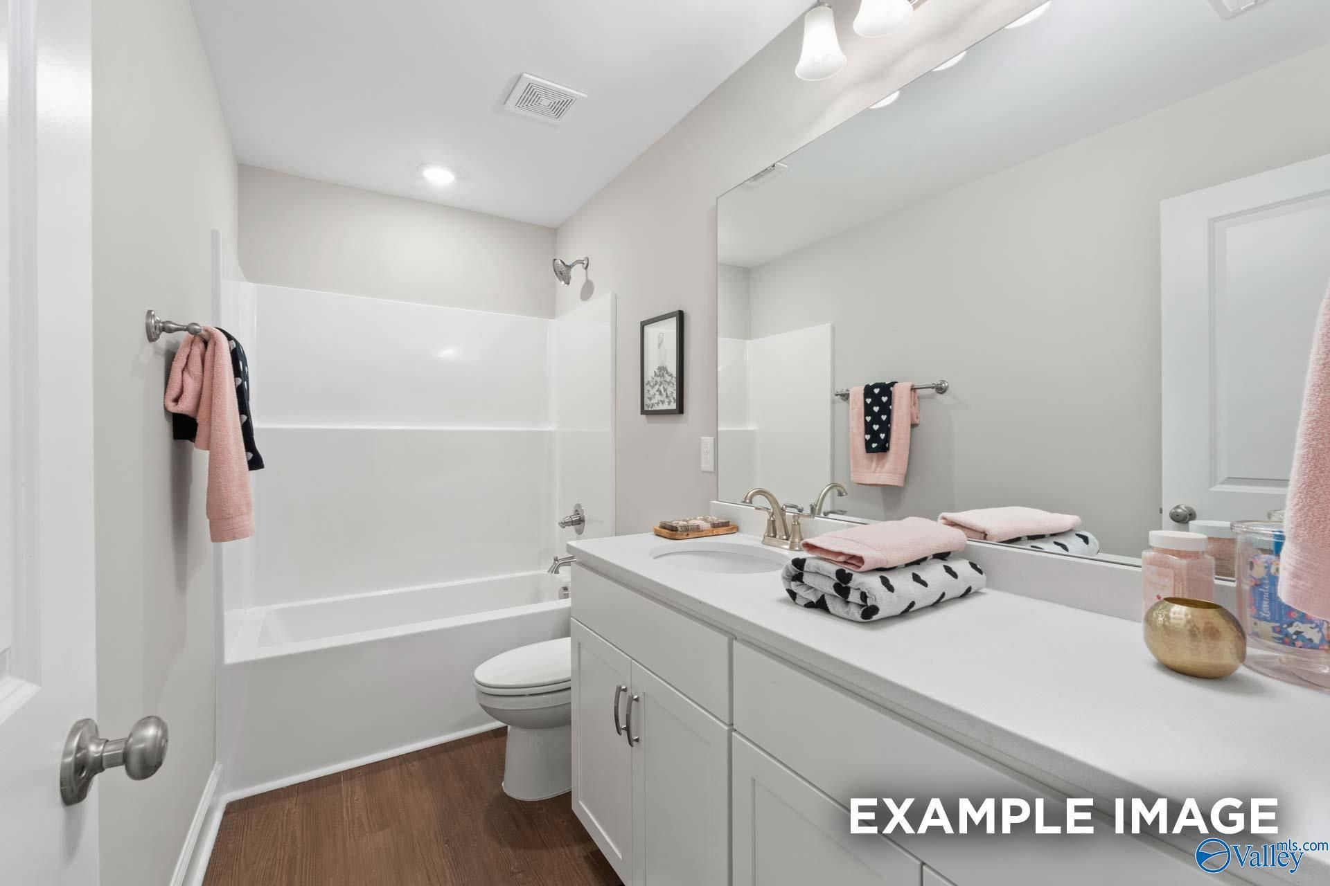 Modern guest bathroom with white tub-shower combo, vanity, mirror, and pink towels in Evermore Homes The Haven E, Owens Cross Roads, AL
