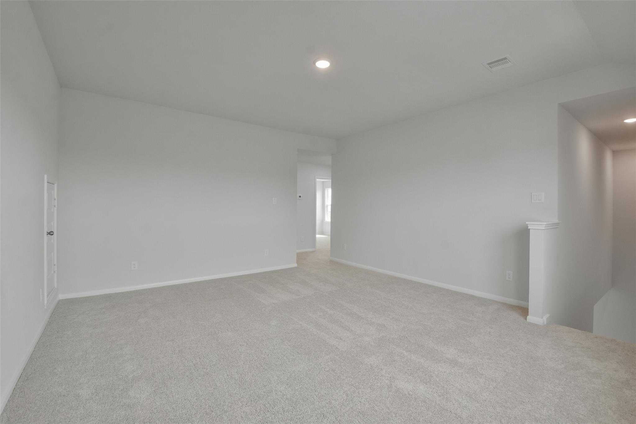 Spacious carpeted living area with white walls, open hallway, and stair railing in Davidson Homes The Tierra A 4-bedroom, Dayton Texas