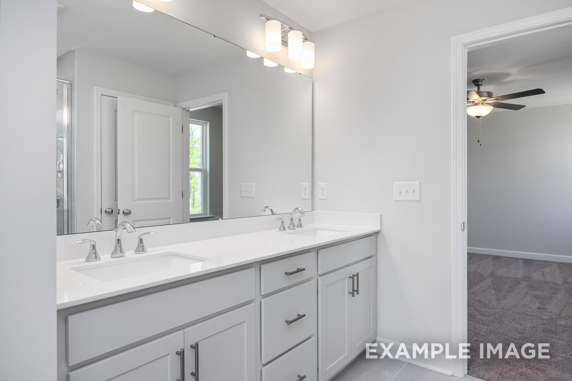 Spacious master bathroom in The Gavin B with white double vanity, large mirror, and adjacent bedroom ceiling fan