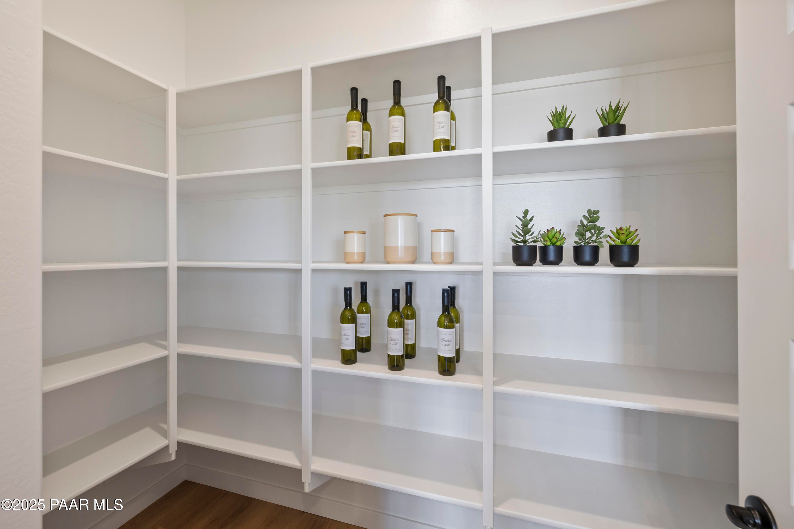 Spacious walk-in pantry with white corner shelving stocked with wine bottles, jars, and potted succulents in Davidson Homes The Blaze D, Prescott