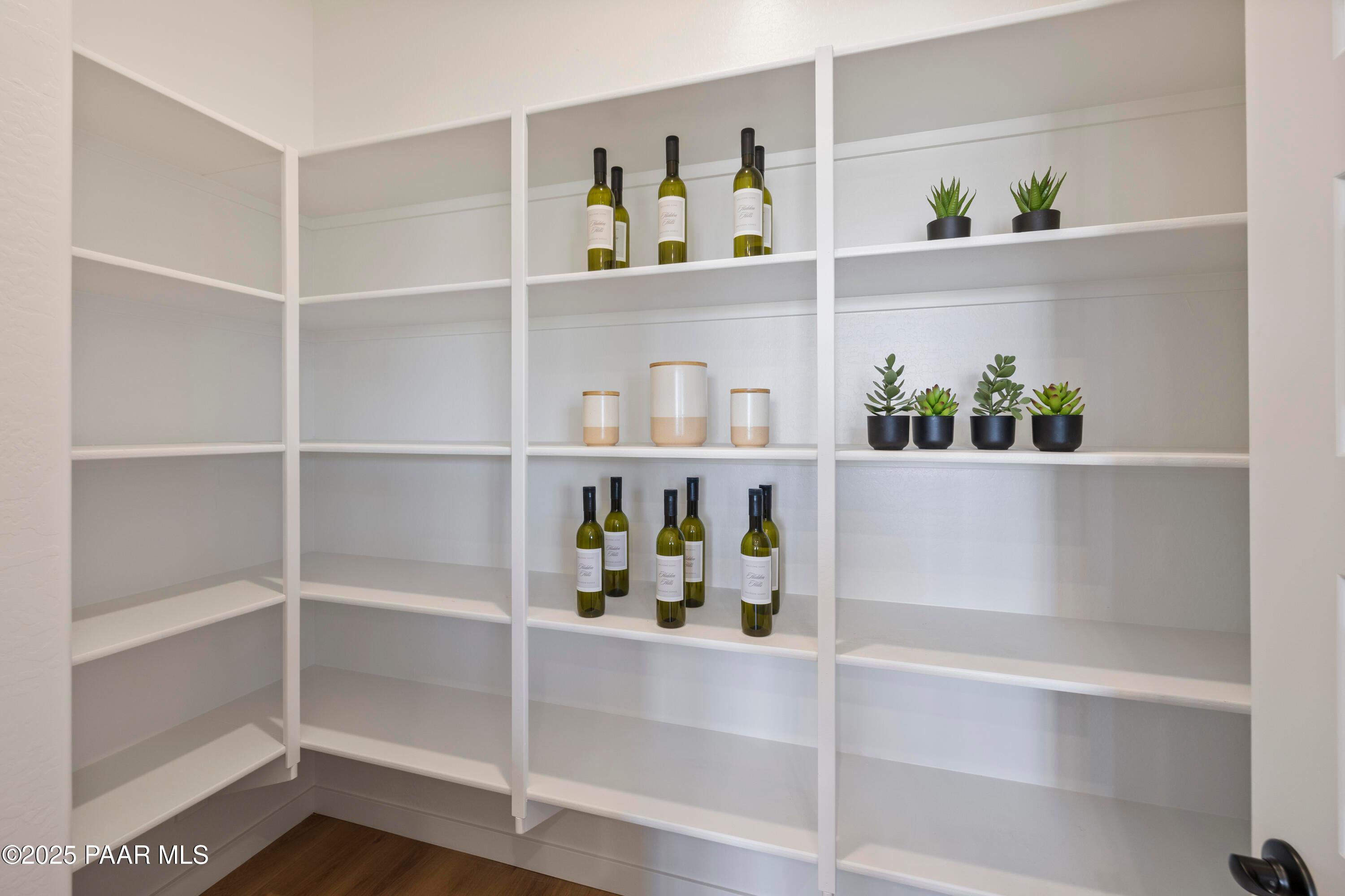 Spacious walk-in pantry with white corner shelving stocked with wine bottles, jars, and potted succulents in Davidson Homes The Blaze D, Prescott