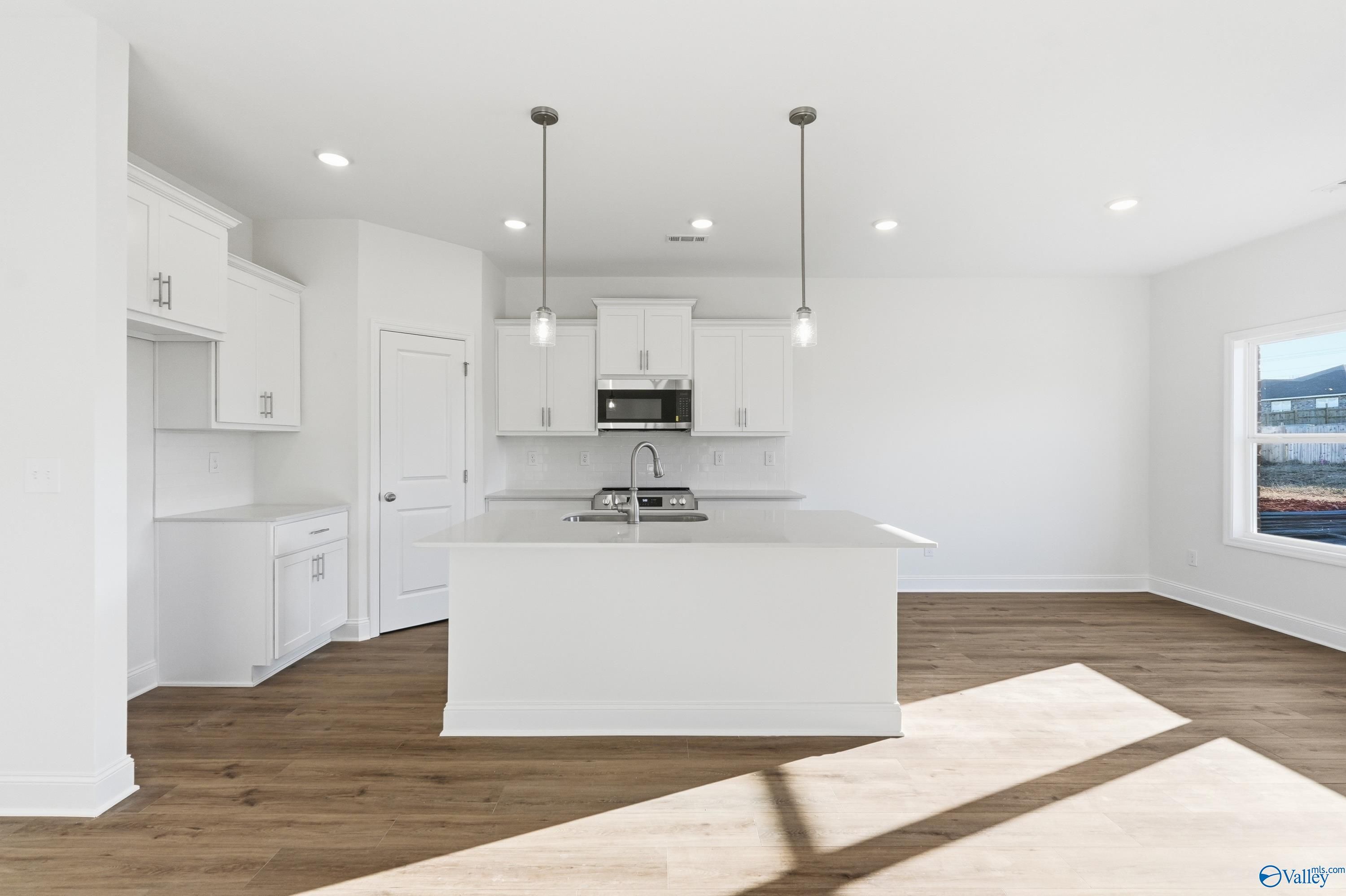 Modern white kitchen island with sink, microwave, and pendant lights in The Asheville C by Davidson Homes, Meridianville, AL