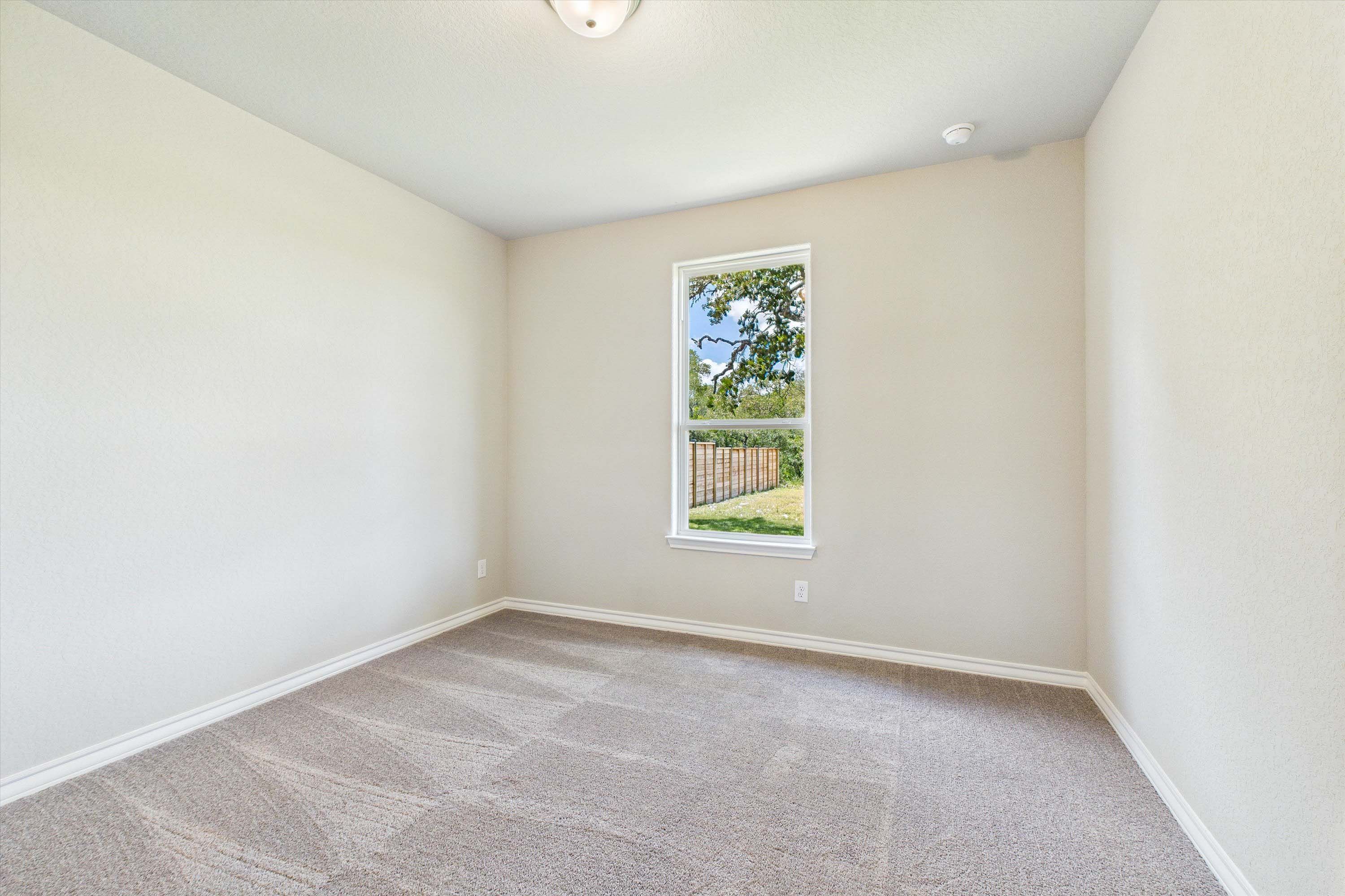 Bright, carpeted bedroom in The Foster home design by Davidson Homes featuring neutral walls and a view of the backyard.