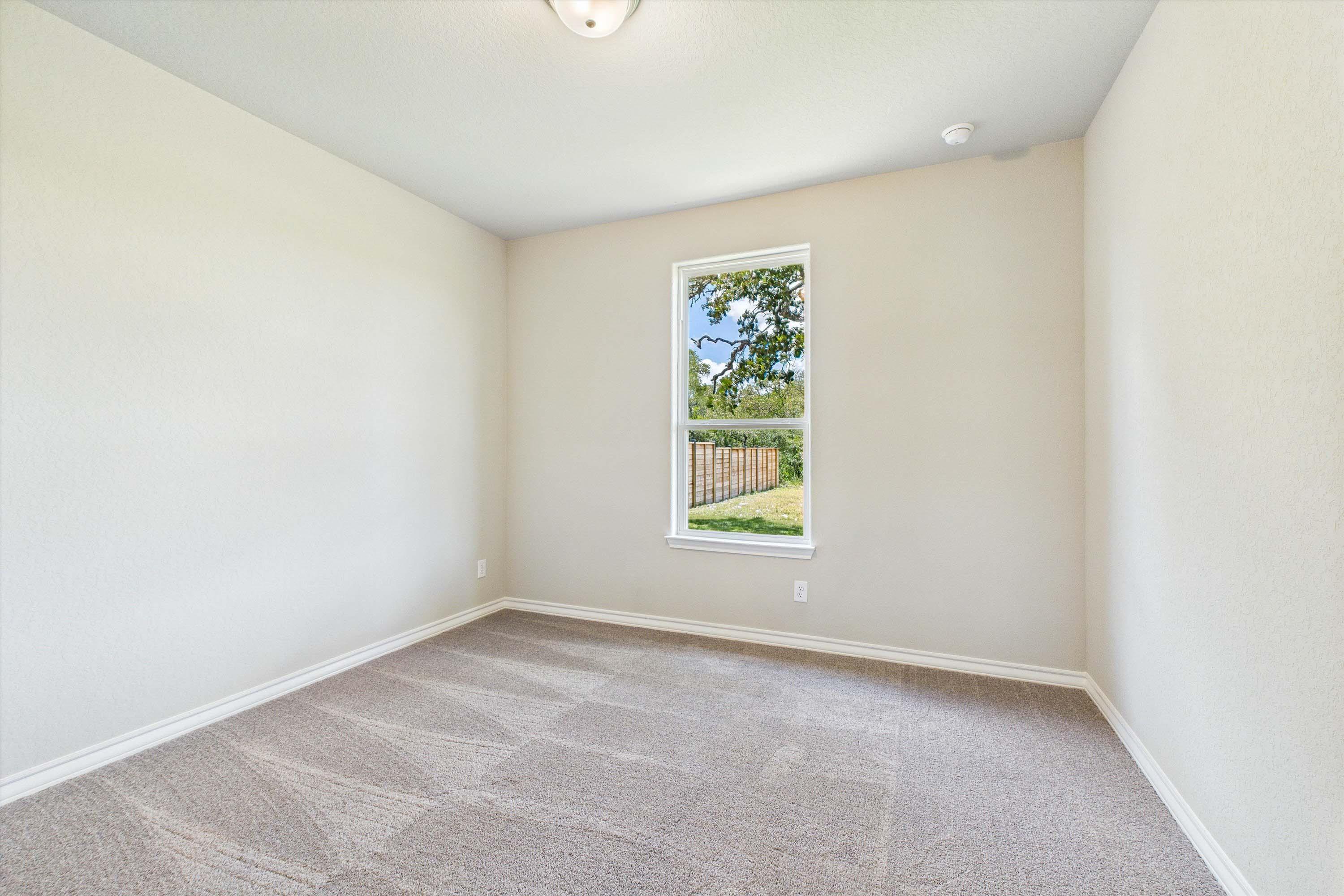 Bright, carpeted bedroom in The Foster home design by Davidson Homes featuring neutral walls and a view of the backyard.