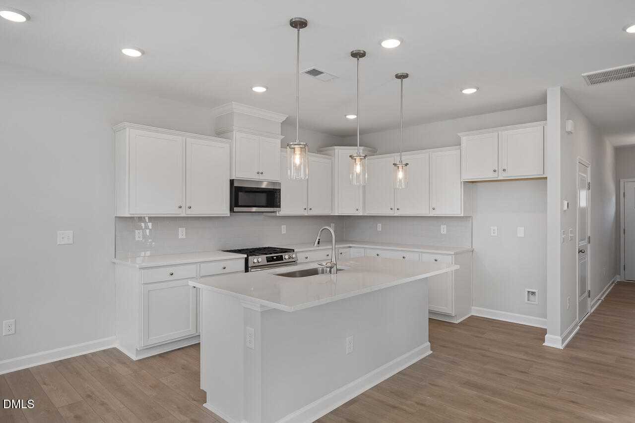 Modern white kitchen with quartz island, undermount sink, stainless microwave, and pendant lights in 3-bed Davidson Homes Graham plan, Fuquay-Varina, NC