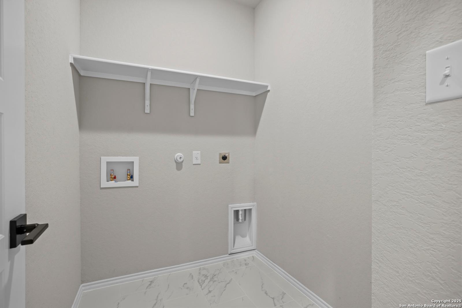 Modern laundry room with white upper shelves, washer-dryer hookups, beige walls in Davidson Homes The Daphne H, Seguin TX