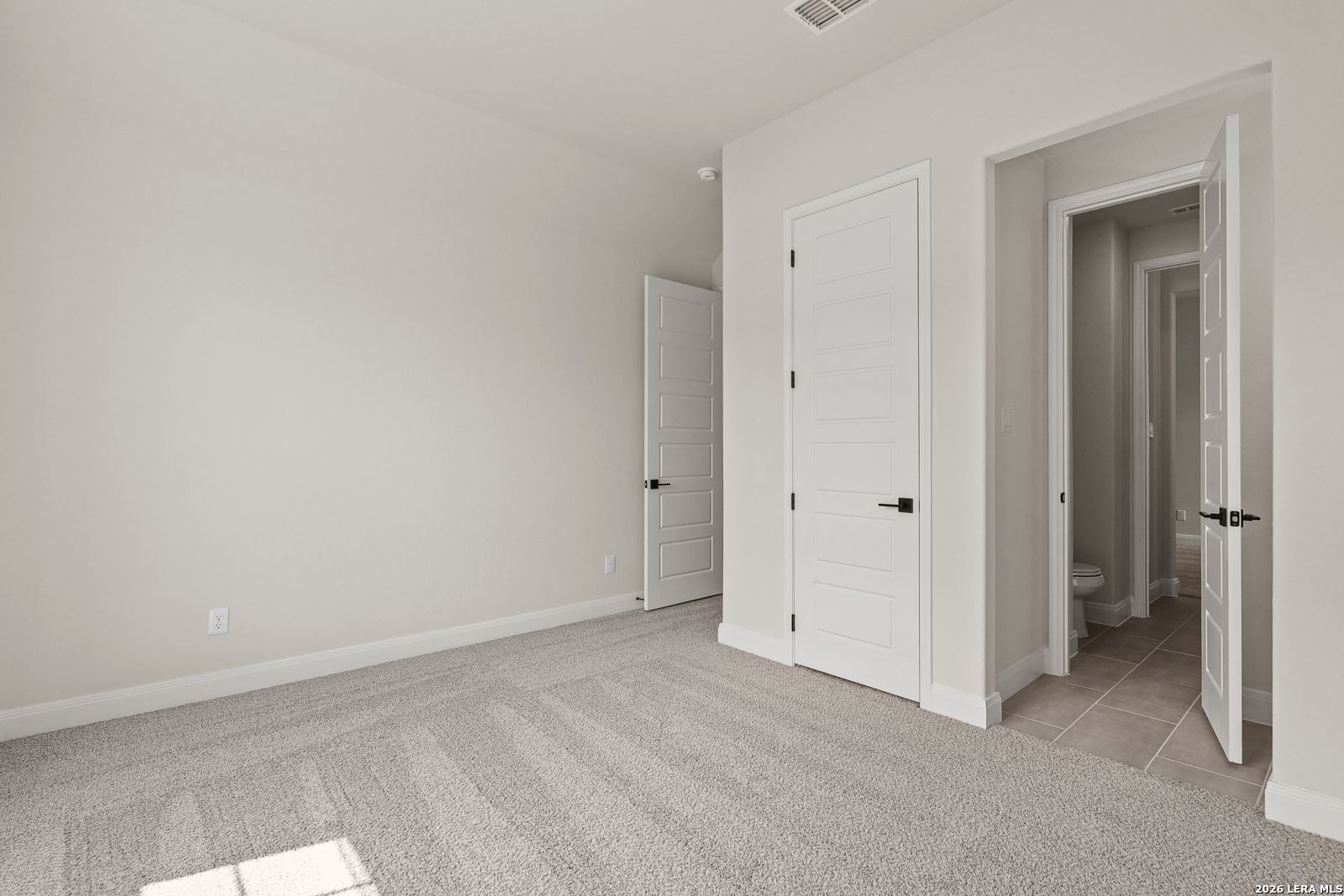Spacious bedroom with neutral carpet and en-suite bathroom in The Summerlin B floor plan at Potranco Oaks, Castroville, Texas.