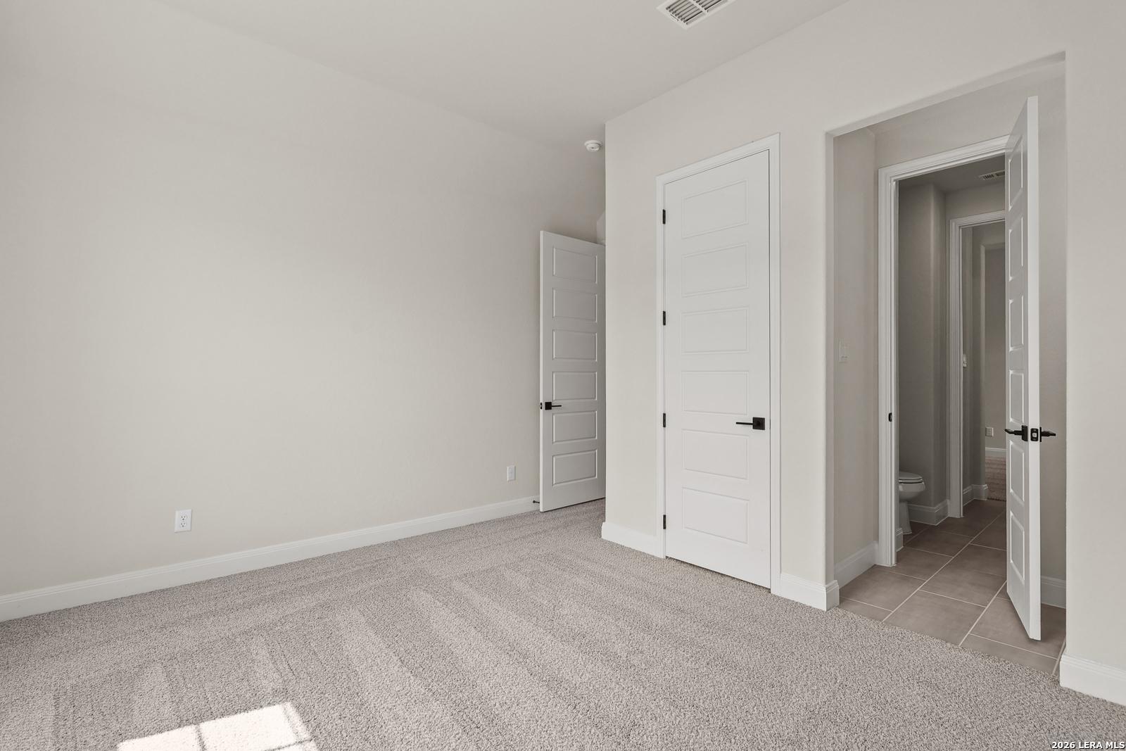 Spacious bedroom with neutral carpet and en-suite bathroom in The Summerlin B floor plan at Potranco Oaks, Castroville, Texas.