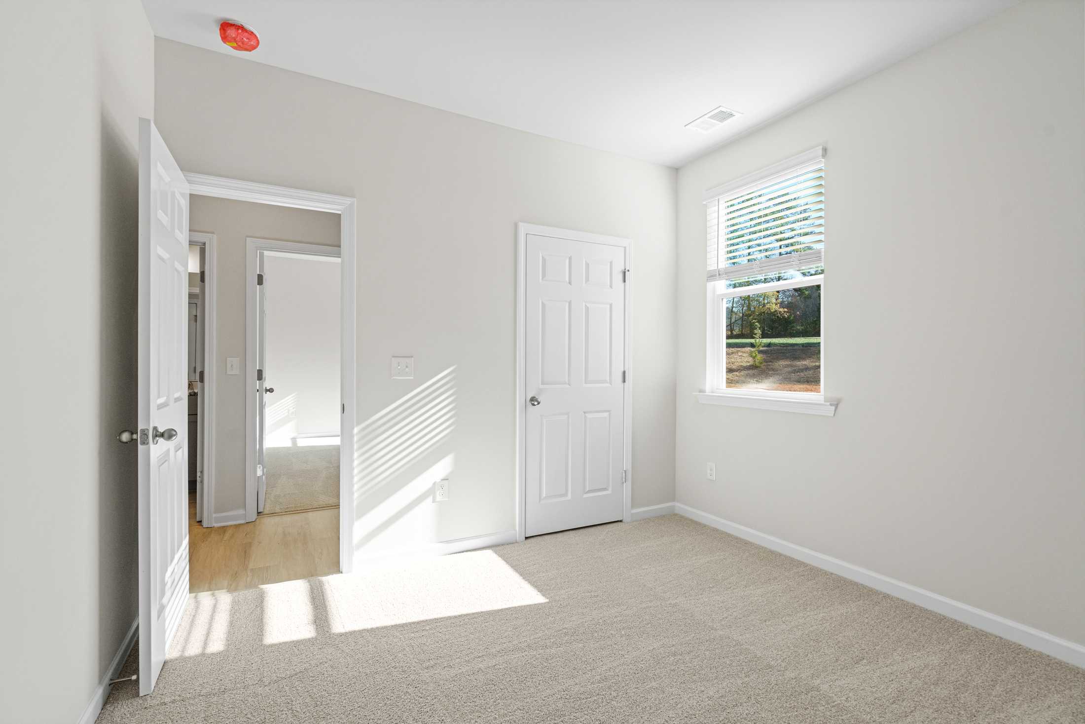 Spacious secondary bedroom in The Glenwood A at Wehunt Meadows, Hoschton GA, with neutral walls, carpeted floor, and window light