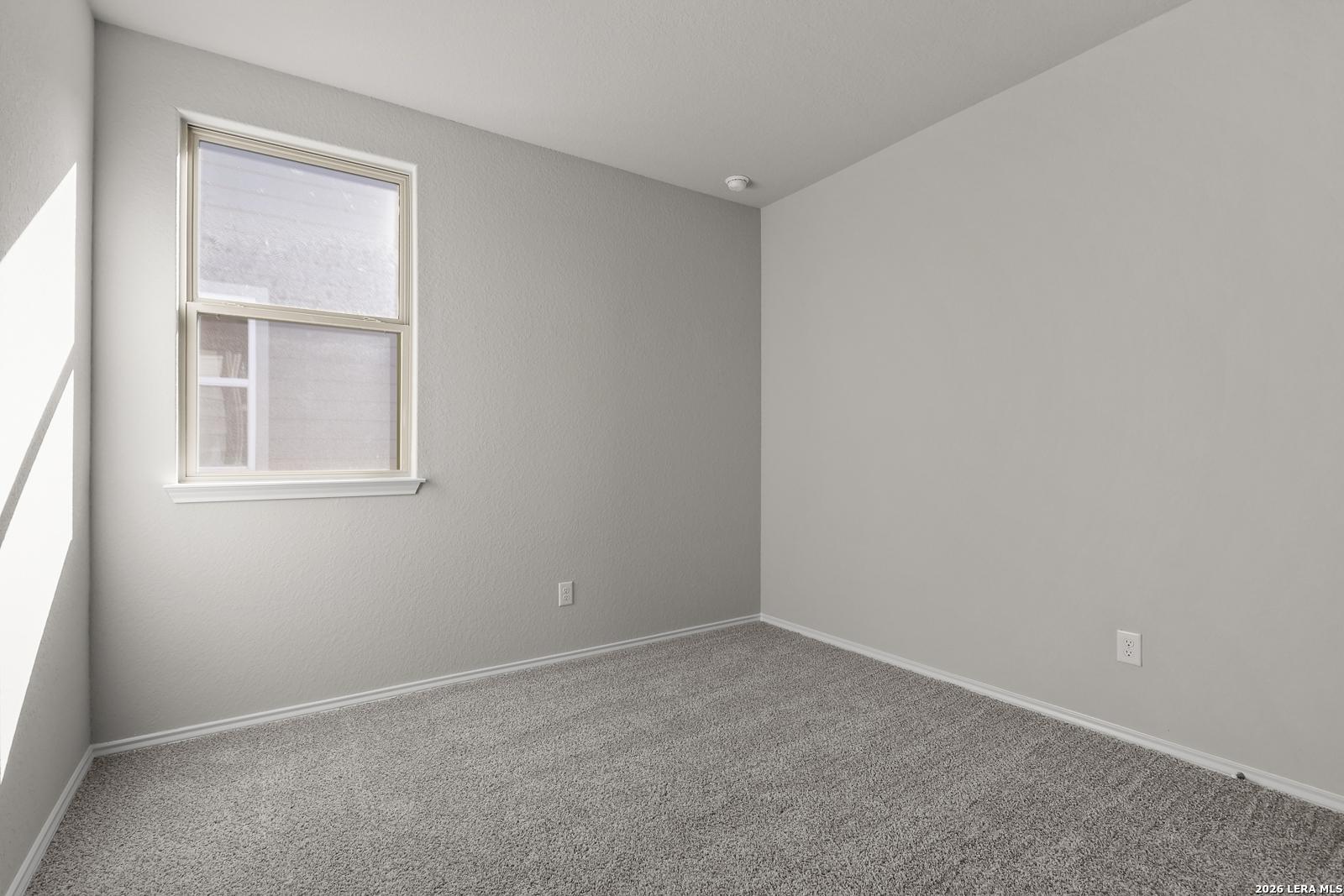 Empty bedroom featuring neutral gray walls, plush carpet, and large window in Davidson Homes The Frio B, San Antonio