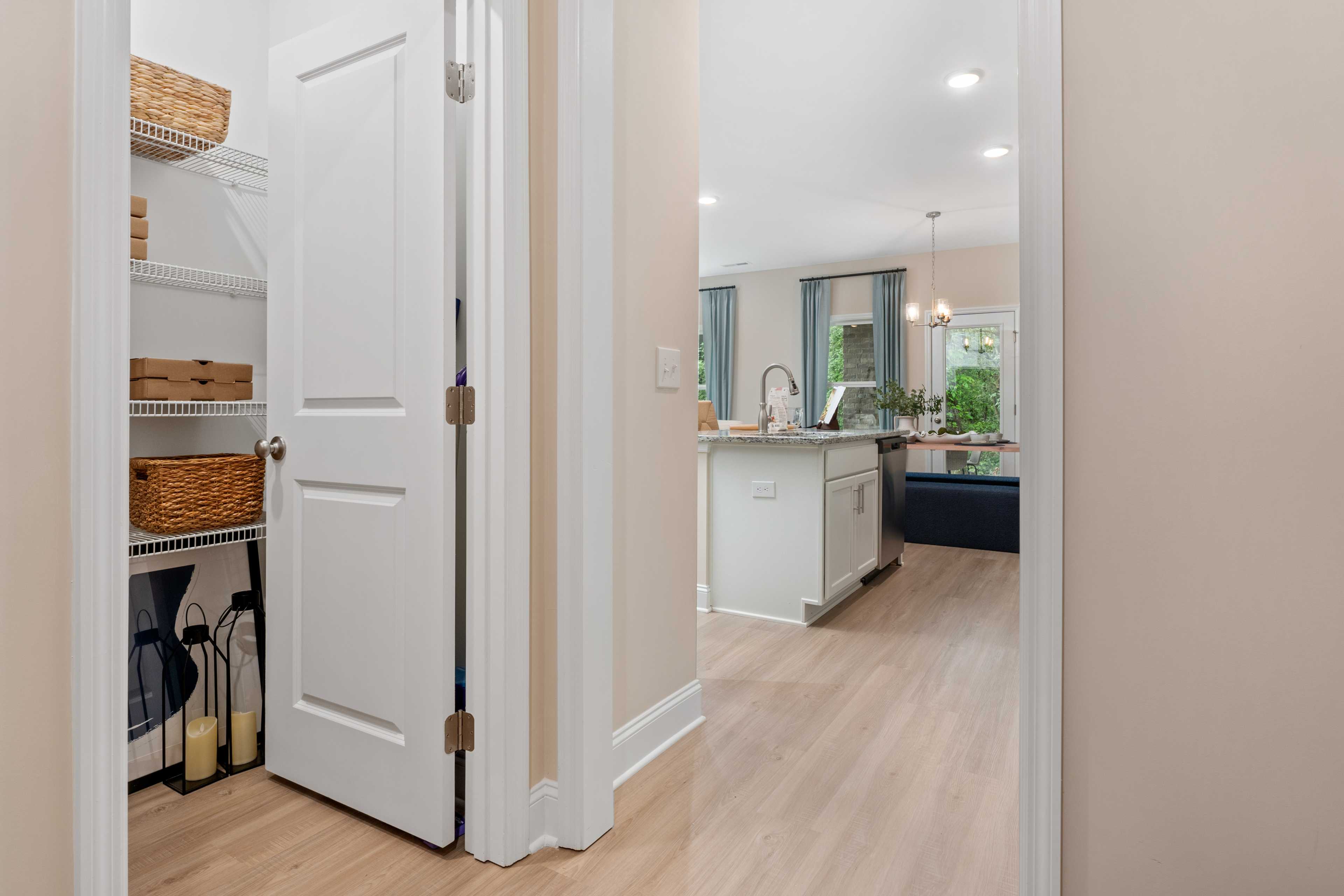 Organized walk-in pantry with wicker baskets and shelves adjacent to modern white kitchen island in Pavilion home, Huntsville AL by Davidson Homes
