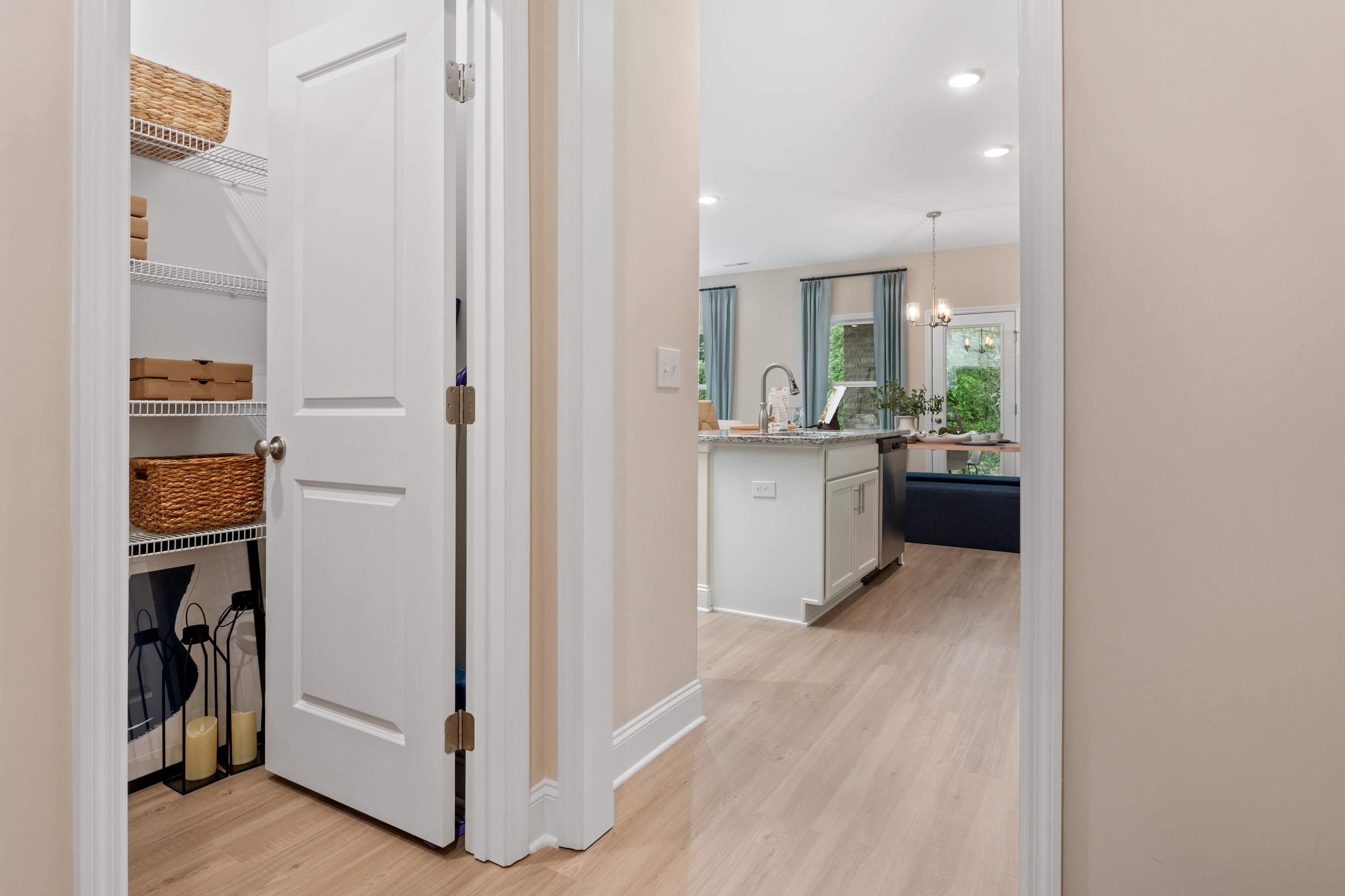 Organized walk-in pantry with wicker baskets and shelves adjacent to modern white kitchen island in Pavilion home, Huntsville AL by Davidson Homes