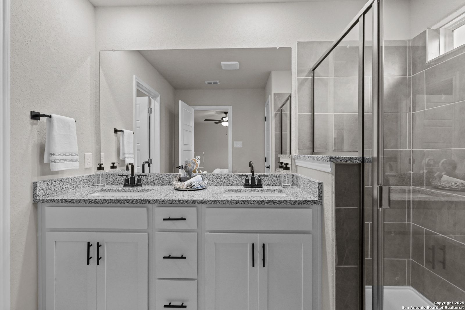 Elegant master bathroom featuring double granite vanity, glass walk-in shower, and white cabinets in Davidson Homes The Charlotte B, San Antonio