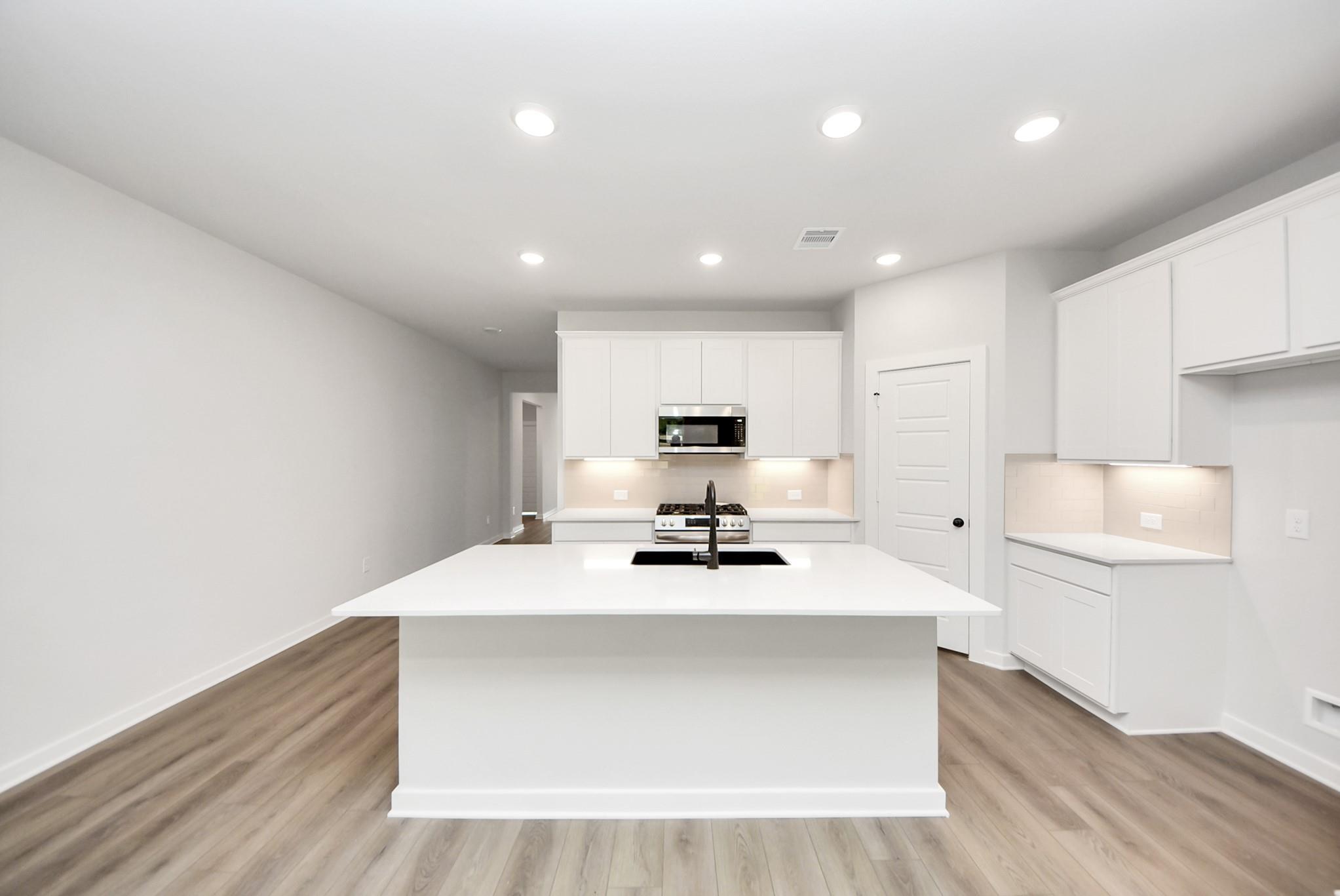 Modern kitchen with white cabinets, large island, and quartz countertops in The Daphne F floor plan at Sundance Cove.