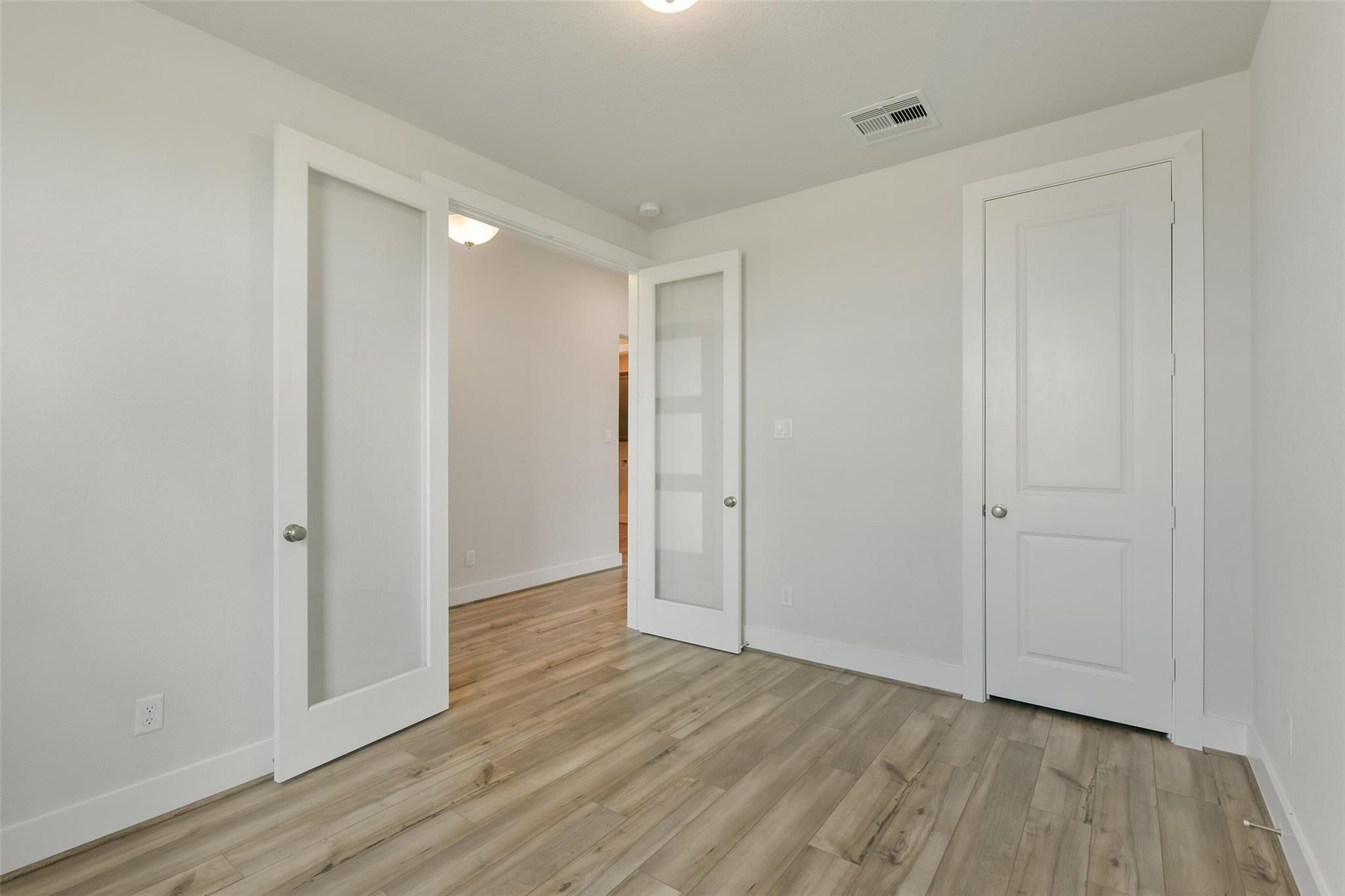 Bright hallway with frosted glass panel doors, white walls, and light hardwood floors in Davidson Homes Edward A, Lago Mar, Texas City