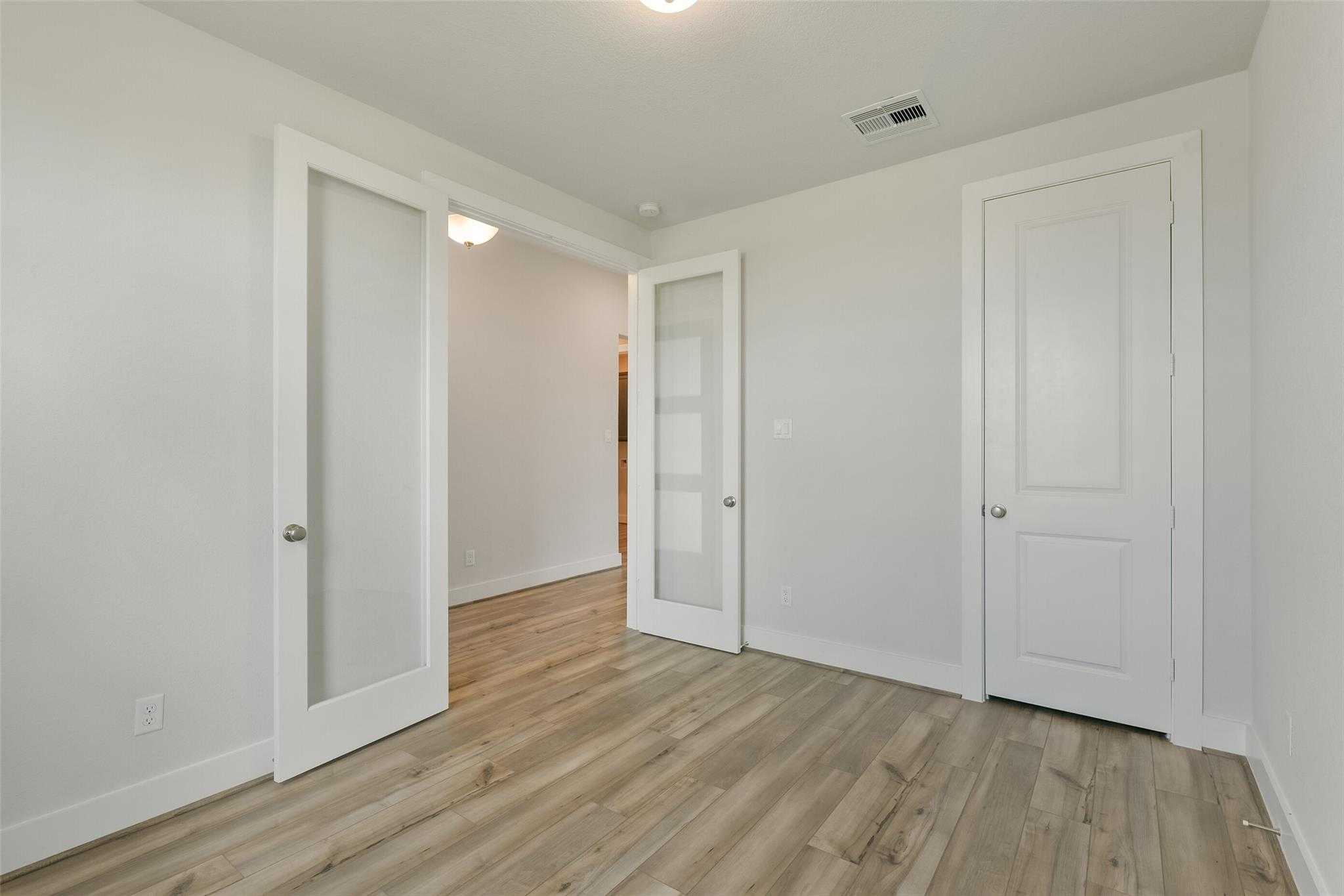 Bright hallway with frosted glass panel doors, white walls, and light hardwood floors in Davidson Homes Edward A, Lago Mar, Texas City