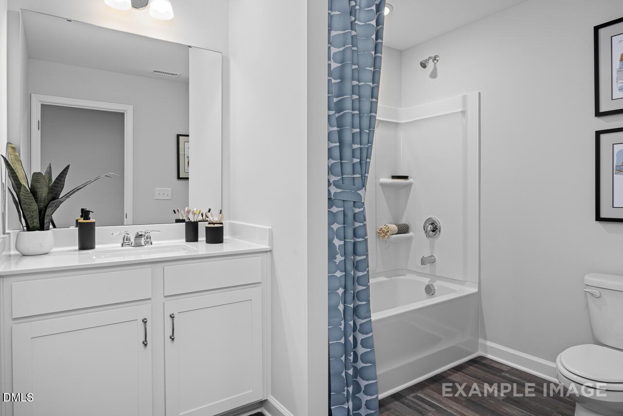 Modern bathroom with double vanity, white cabinets, blue shower curtain, tub, and plants in Davidson Homes Magnolia D, Angier, NC