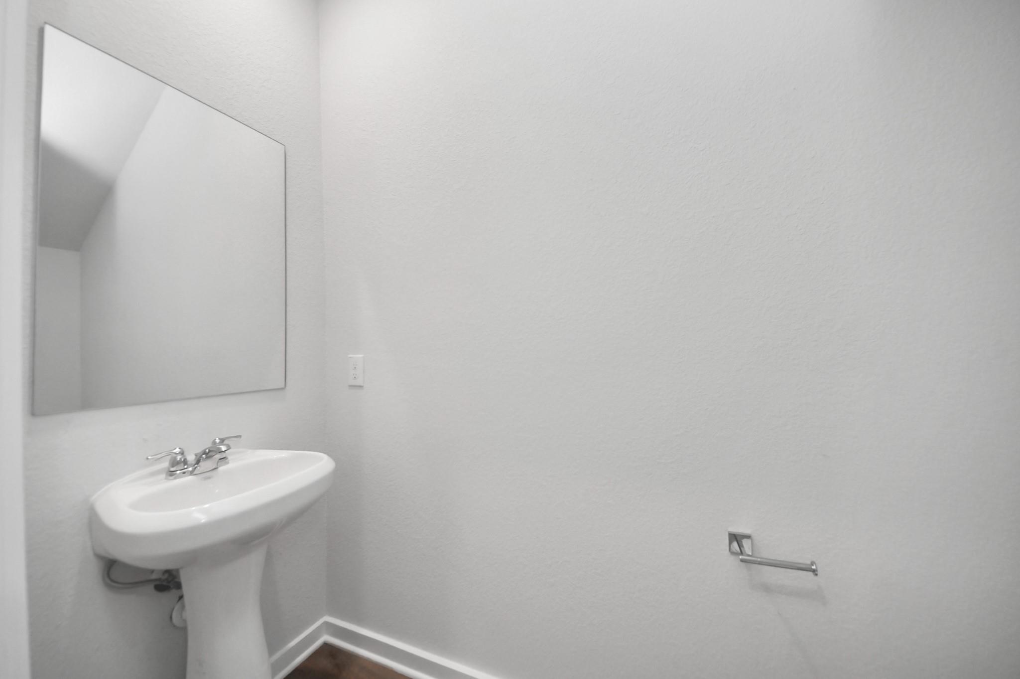 Modern powder room with pedestal sink and wall mirror in The Brazos F floor plan at Liberty Estates, Cleveland, Texas.