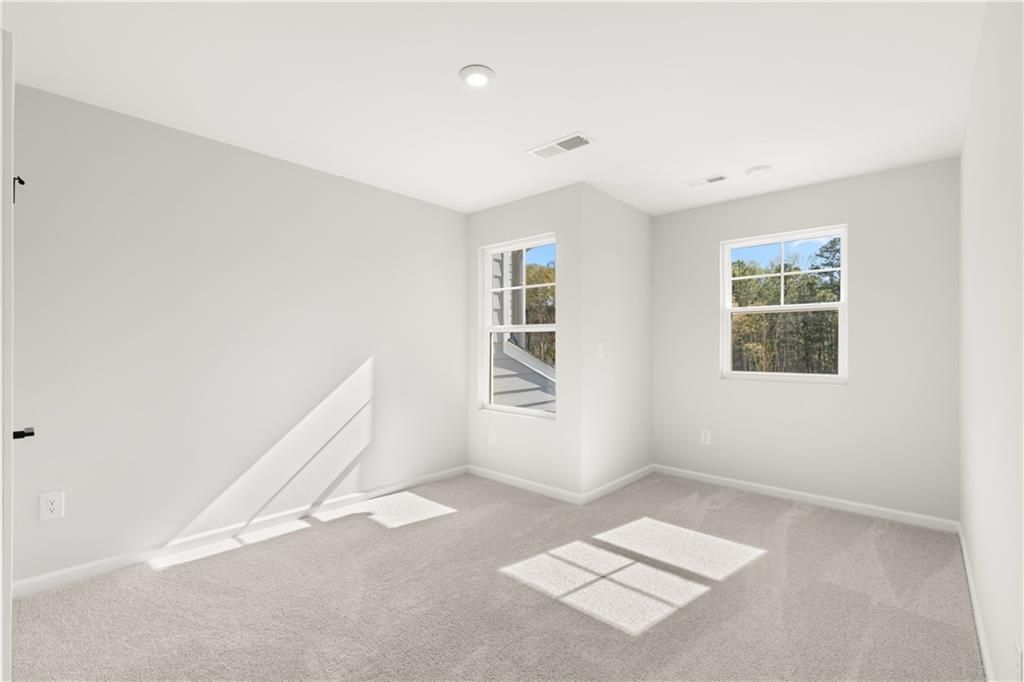 Bright empty bedroom with light gray walls, plush carpet, and sunny double windows in Davidson Homes The Cary A, Winder, Georgia