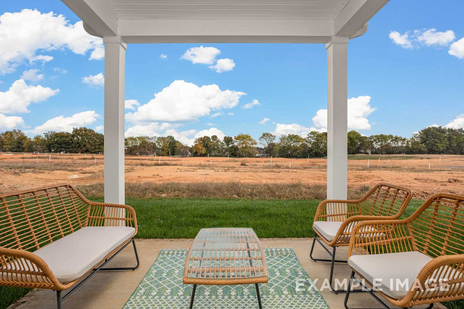 Spacious covered porch of The Gordon B with rattan furniture, glass table, and scenic field view under blue skies