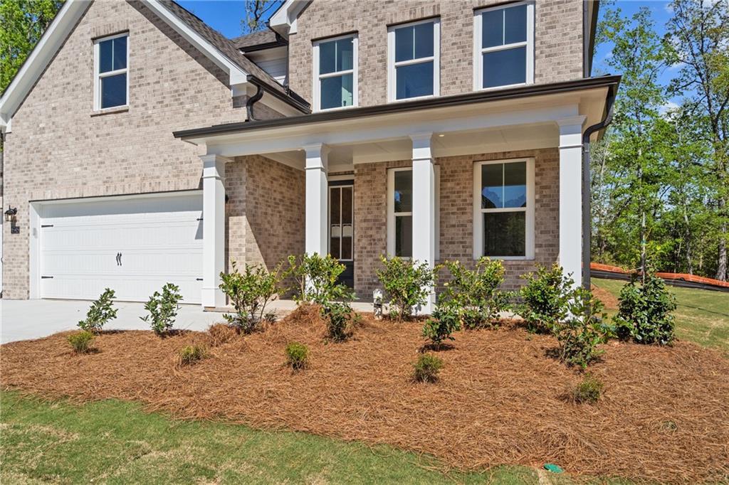 Two-story brick home with covered porch, three-car garage, and landscaped shrubs in Davidson Homes The Hickory E, Buford, Georgia