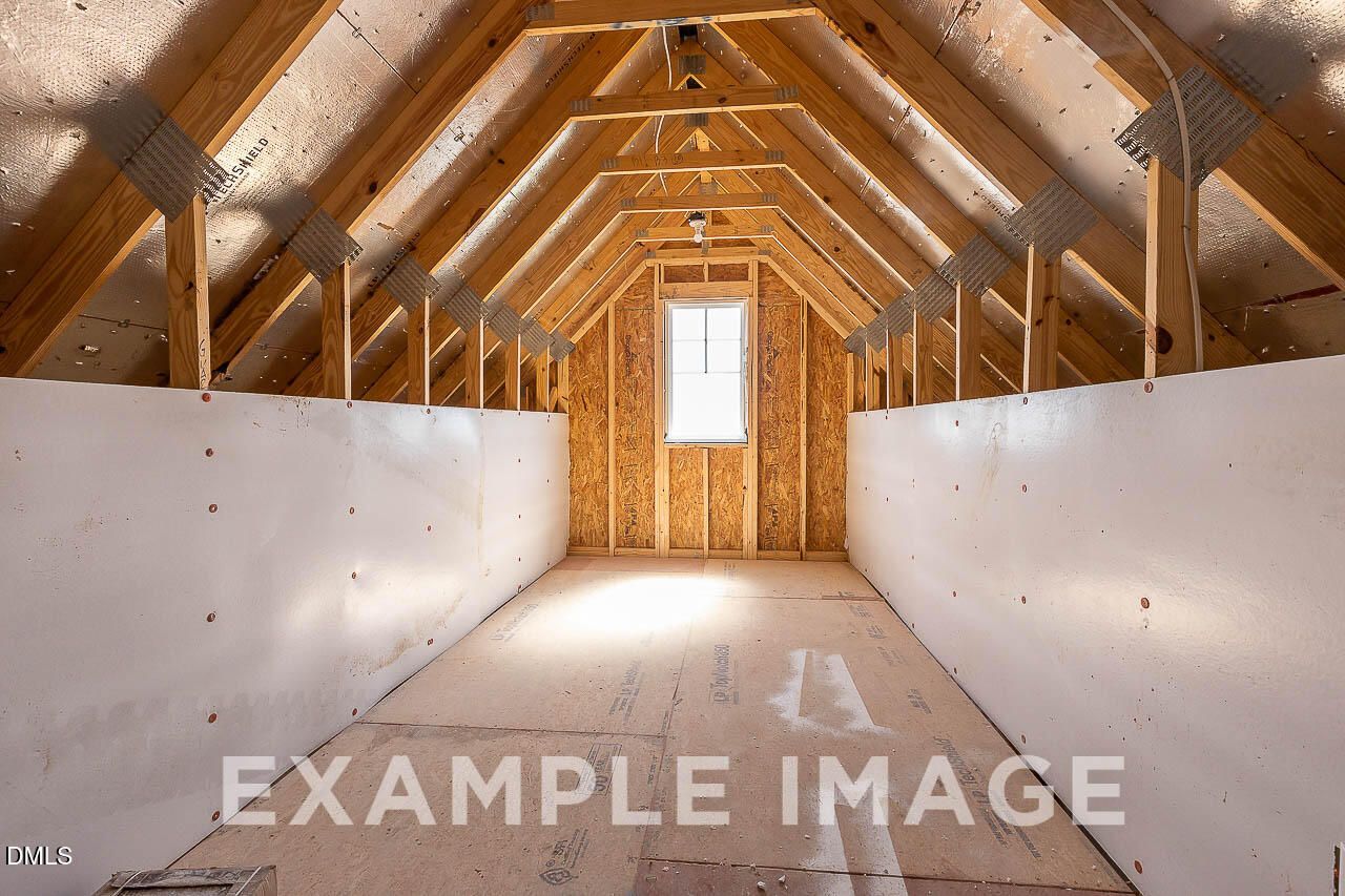 Unfinished attic storage space with exposed wood trusses and window in Davidson Homes The Ash C, Retreat at North Main, Lillington NC