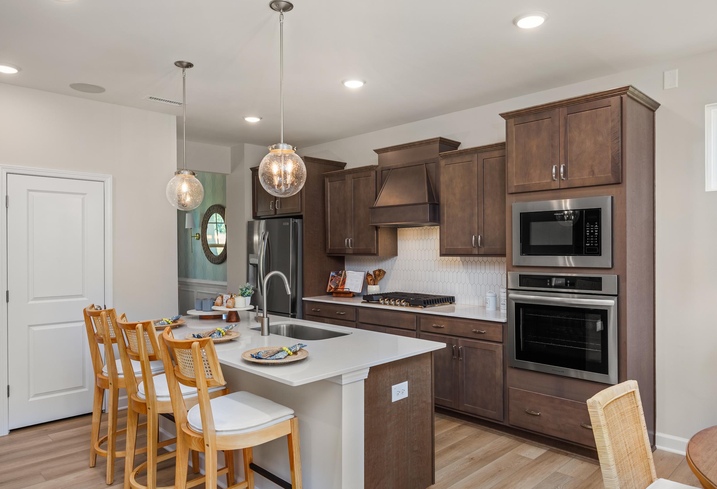 Spacious gourmet kitchen in The Willow G featuring dark wood cabinets, white quartz island, and stainless steel appliances