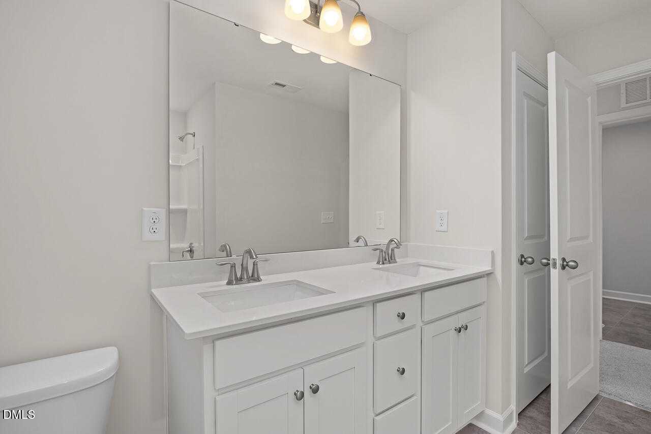 Modern master bathroom featuring double vanity sinks, white shaker cabinets, and frameless mirror in Davidson Homes The Warren, Fuquay-Varina, NC