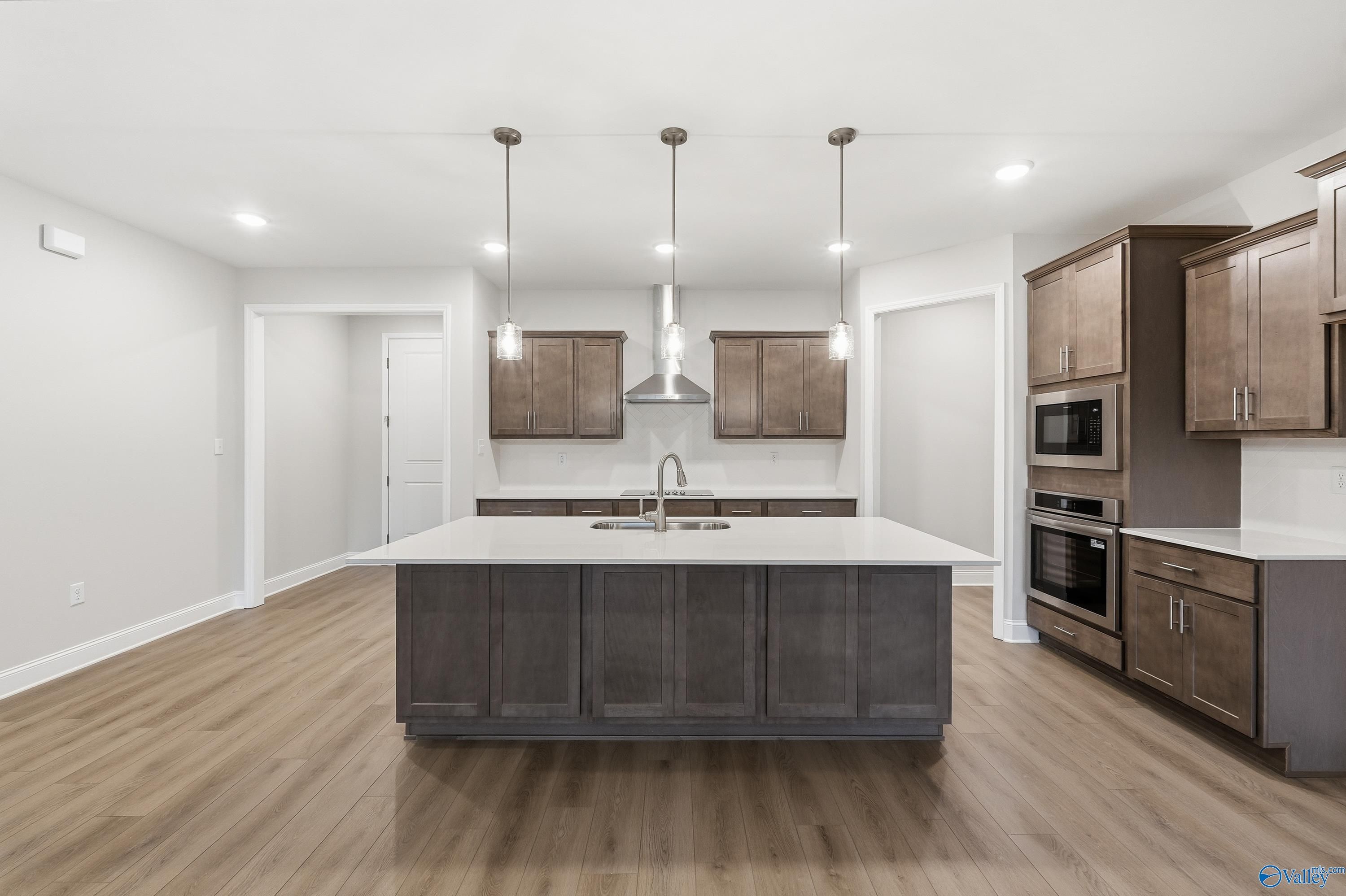 Modern kitchen featuring large island sink, shaker cabinets, and pendant lights in The Kirkland 3-bedroom home, Decatur, Alabama