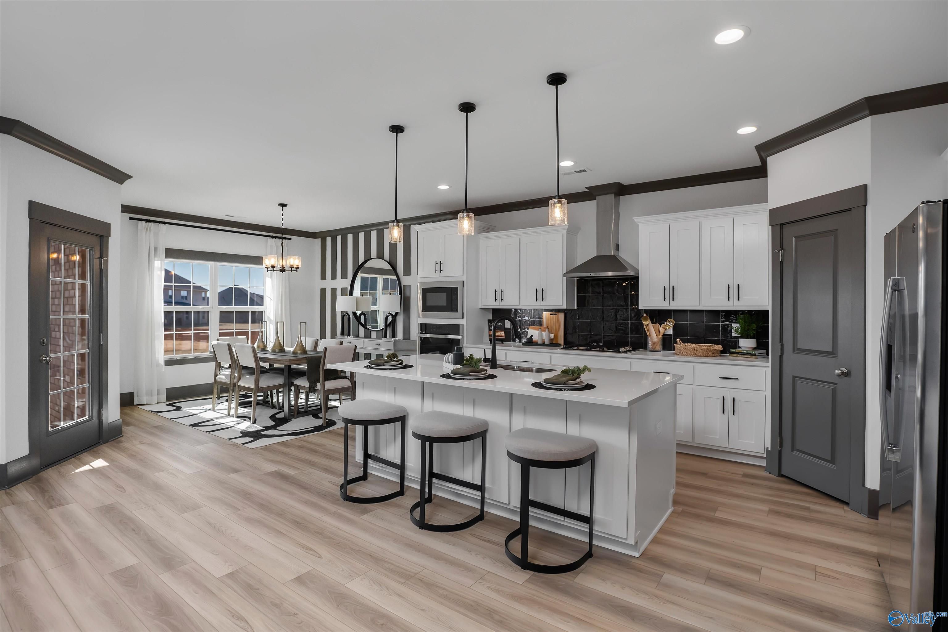 Open-concept kitchen with white shaker cabinets, stainless appliances, island bar stools, and dining area in Davidson Homes The Rockford B, Madison AL