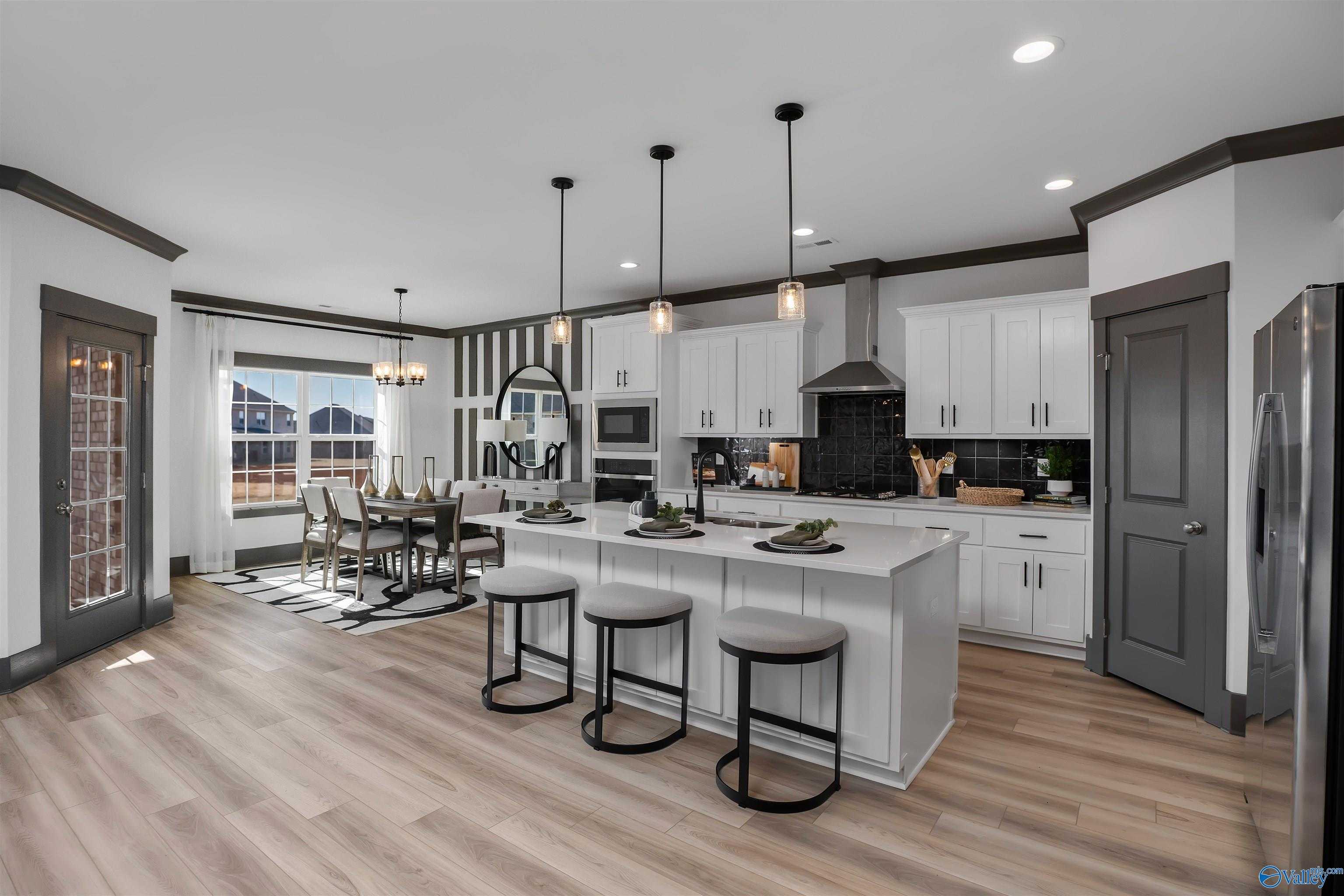 Open-concept kitchen with white shaker cabinets, stainless appliances, island bar stools, and dining area in Davidson Homes The Rockford B, Madison AL