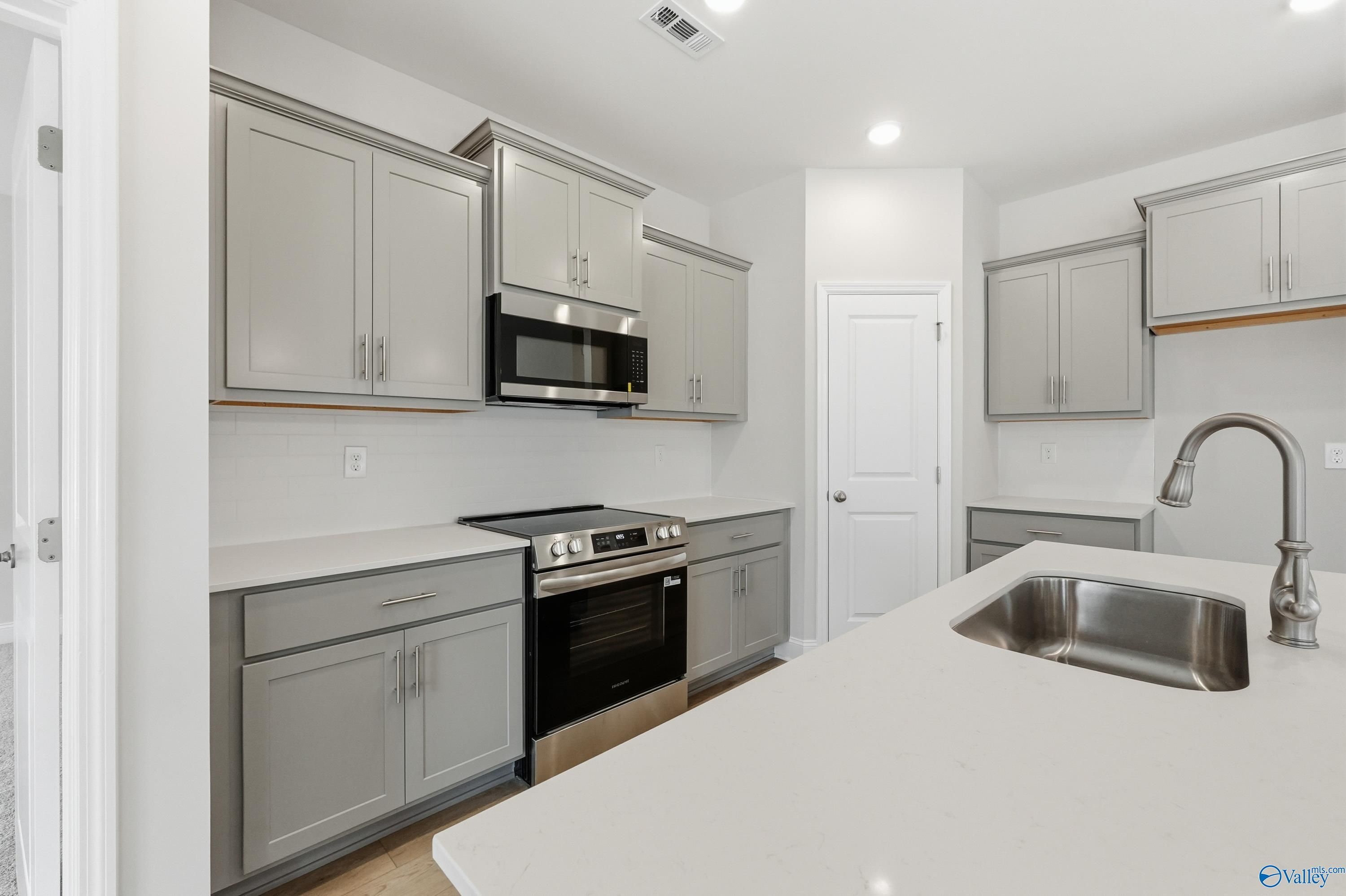 Modern gray shaker kitchen with white quartz counters, stainless appliances, and island in Davidson Homes The Franklin, Meridianville AL