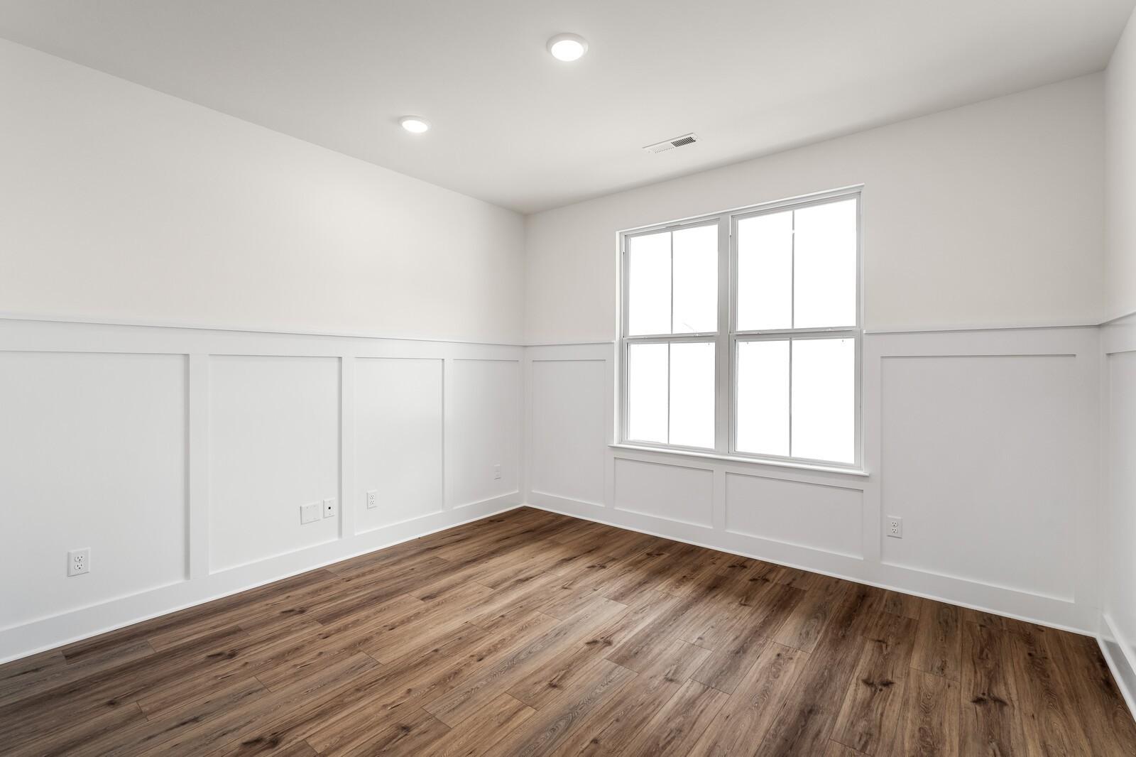 Bright empty bedroom featuring white wainscoting, large window, hardwood floors in Davidson Homes The Ridgeport, Gallatin, TN