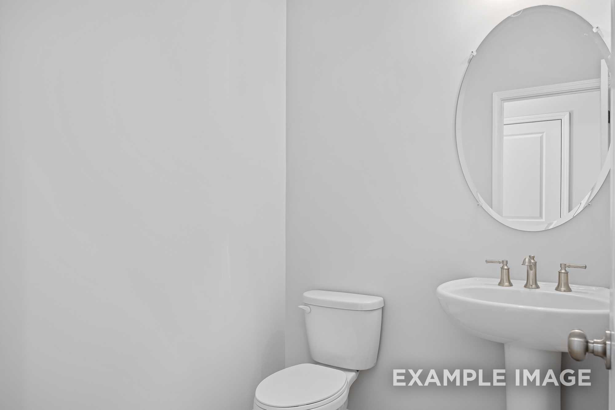 Modern powder room in The Cypress D II featuring round mirror, pedestal sink, toilet, and white walls by Davidson Homes in Angier NC