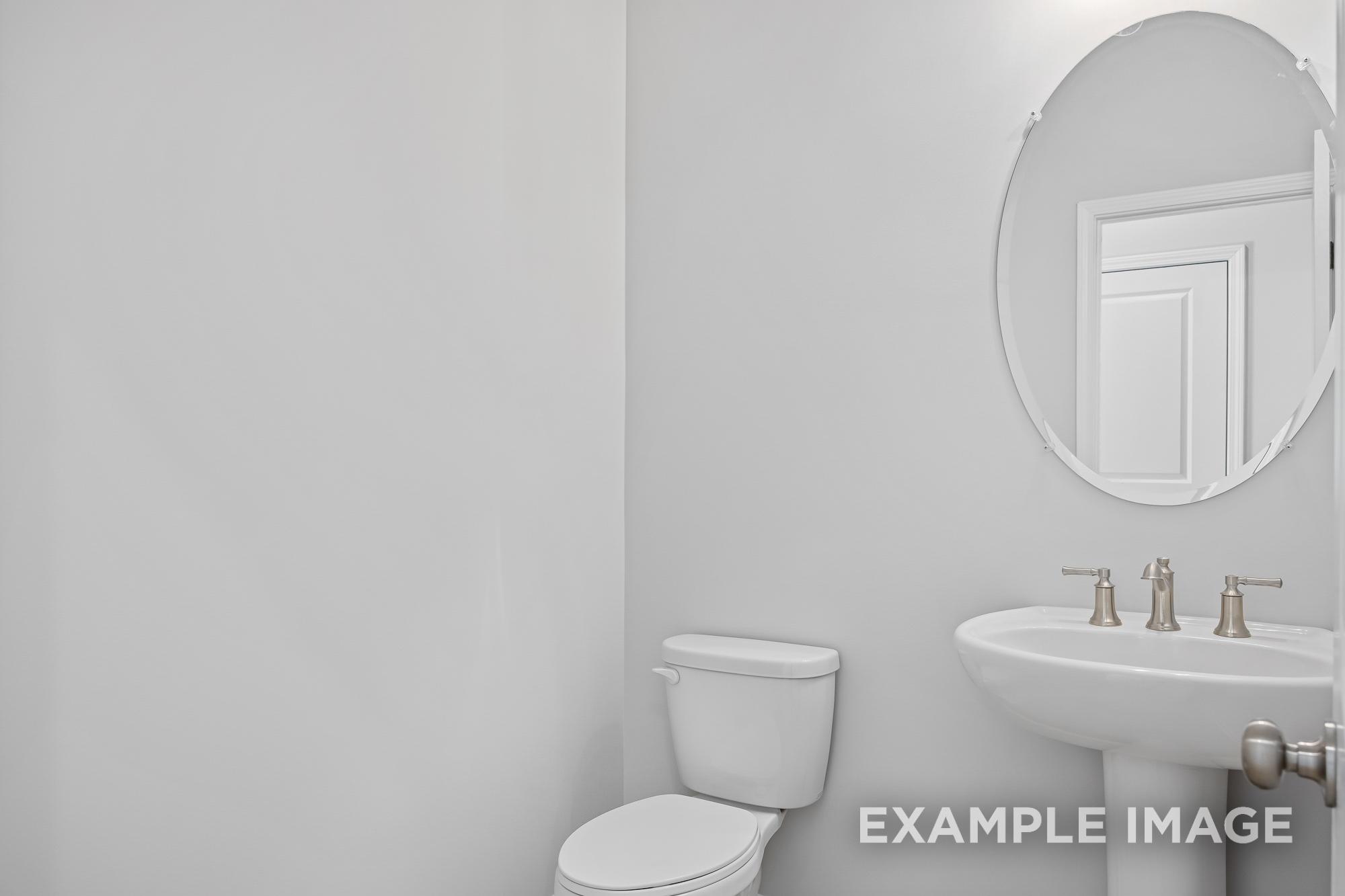 Spacious powder room in The Cypress C II with round mirror, pedestal sink, chrome faucet, and white toilet
