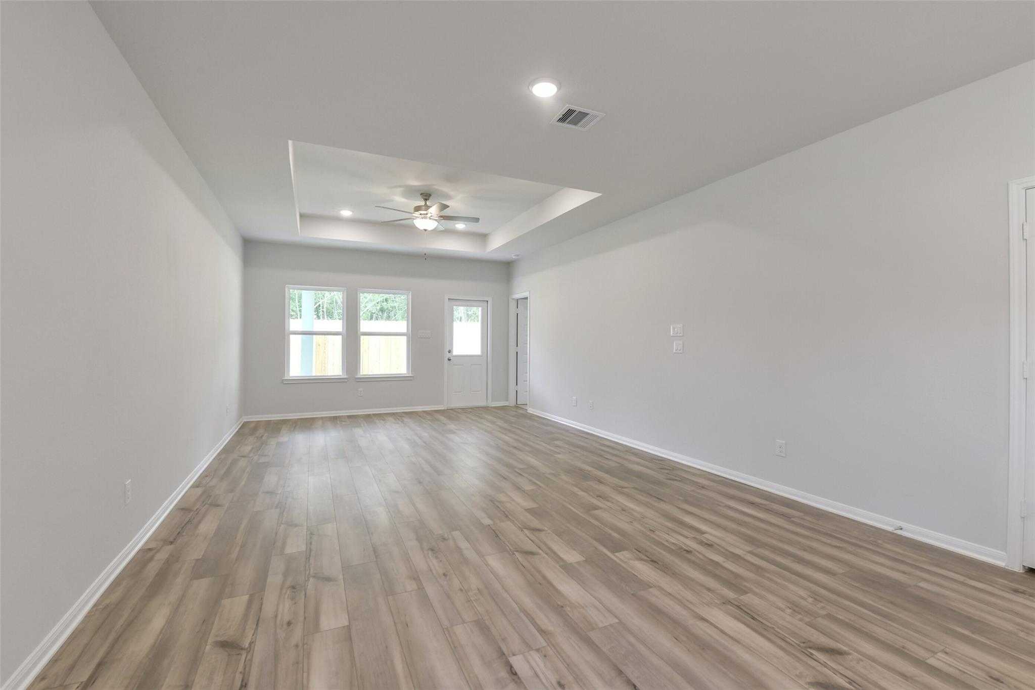Bright open living room with light hardwood floors, large windows, tray ceiling fan in Davidson Homes The Frio G, Conroe, Texas