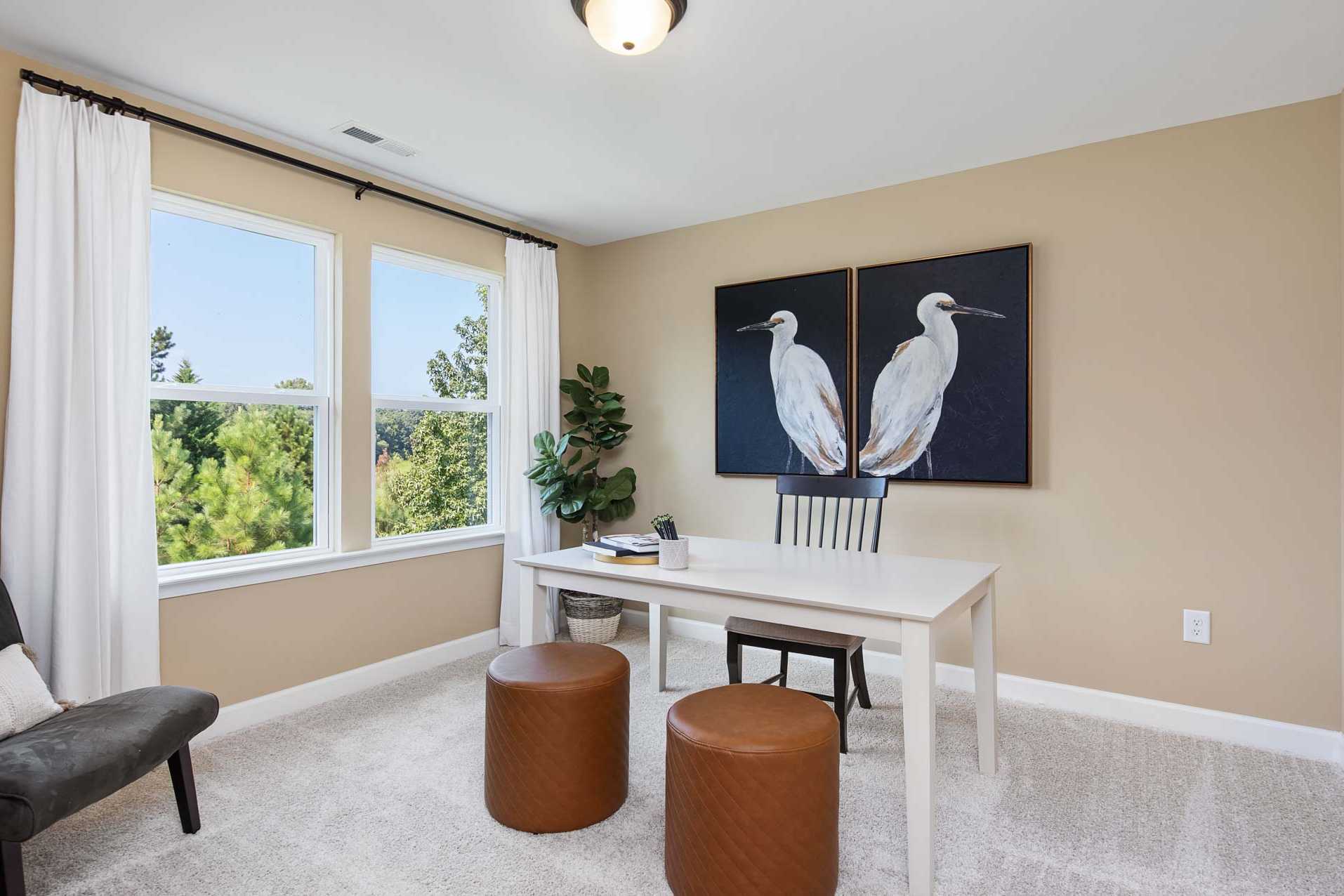 Cozy home office at Sierra Heights in Clayton NC with large windows, egret wall art, wooden desk, leather stools, and potted plant