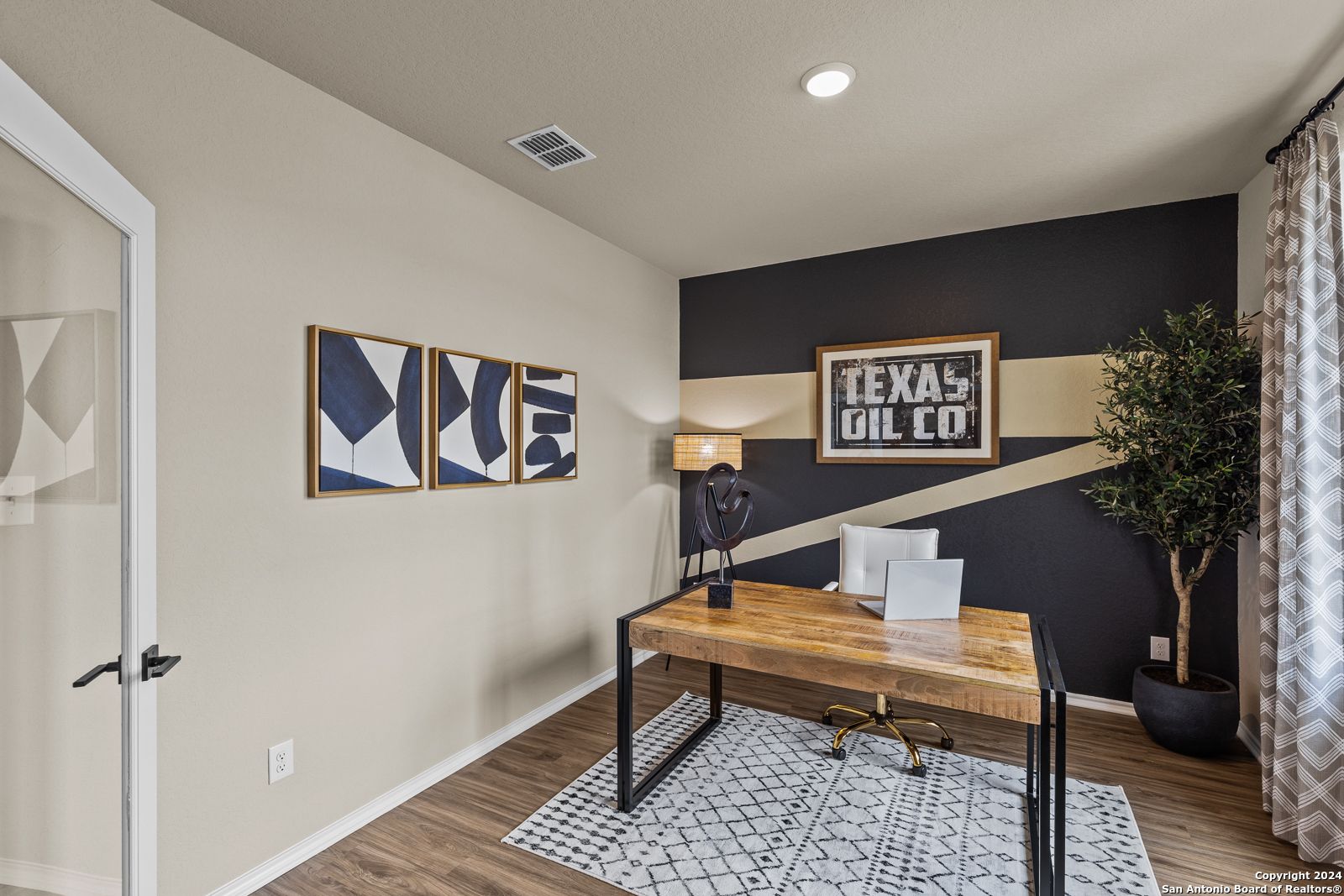 Modern home office with reclaimed wood desk, abstract wall art, Texas Oil Co. sign, and potted plant in Davidson Homes The Douglas F, San Antonio