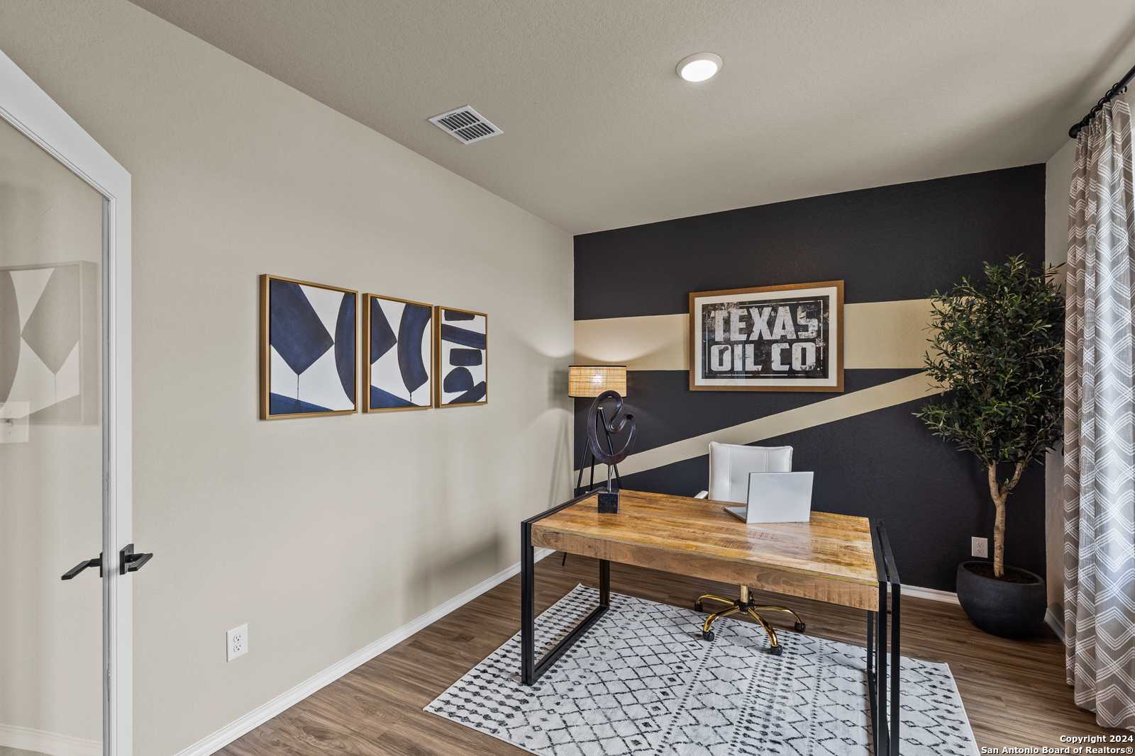 Modern home office with reclaimed wood desk, abstract wall art, Texas Oil Co. sign, and potted plant in Davidson Homes The Douglas F, San Antonio