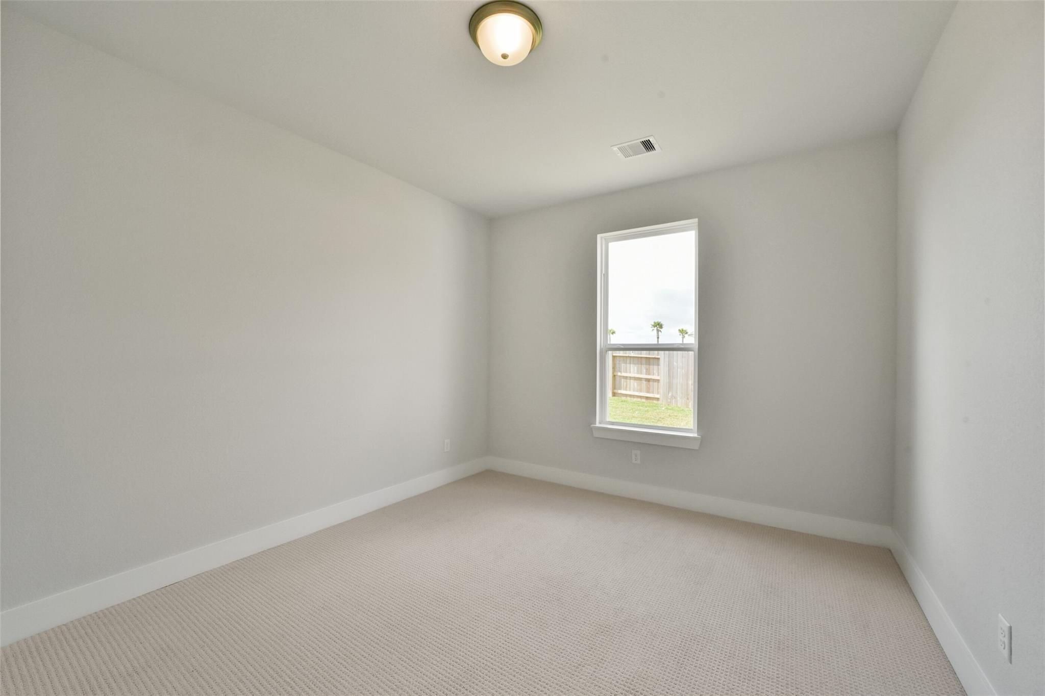 Empty bedroom with light gray walls, large window overlooking yard, beige carpet in Davidson Homes The Zion A, Lago Mar, Texas City