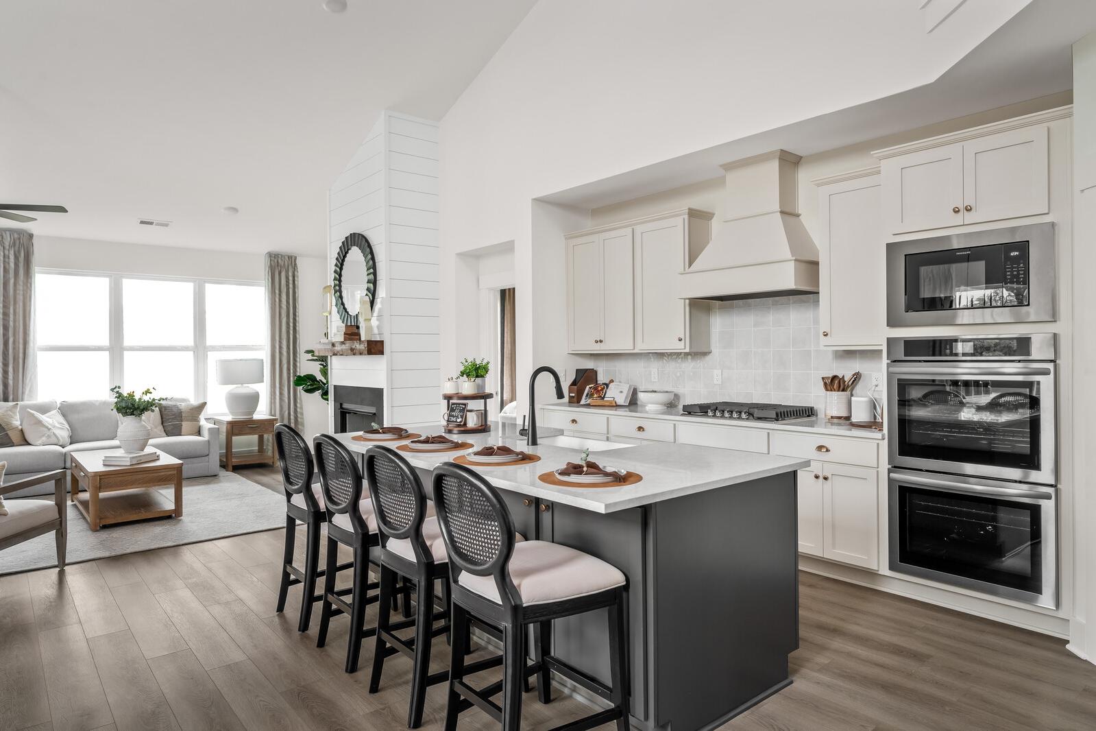 Open-concept kitchen and living area at Woods Crossing in Gallatin TN with white cabinets, gray island, bar stools, and shiplap fireplace
