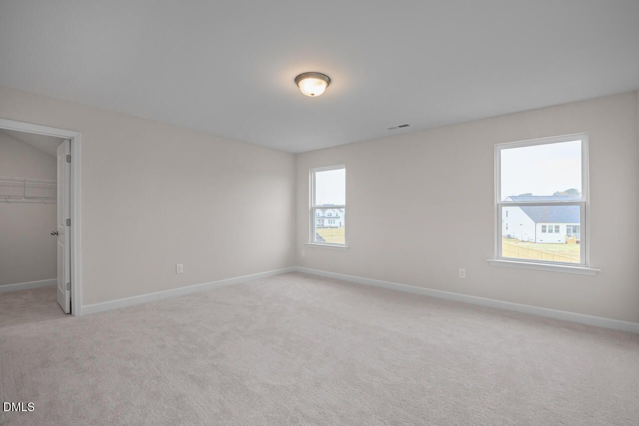 Bright empty bedroom with beige walls, carpet floor, walk-in closet, and dual windows in Davidson Homes The Cypress D II, Angier, NC