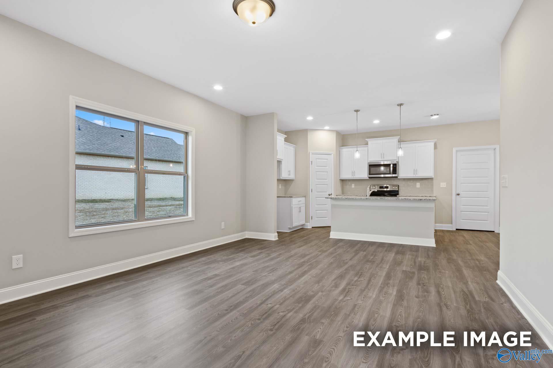 Open-concept kitchen and living room with white cabinets, granite island, hardwood floors, and large windows in 2-bedroom Camilla A home, Hartselle, Alabama