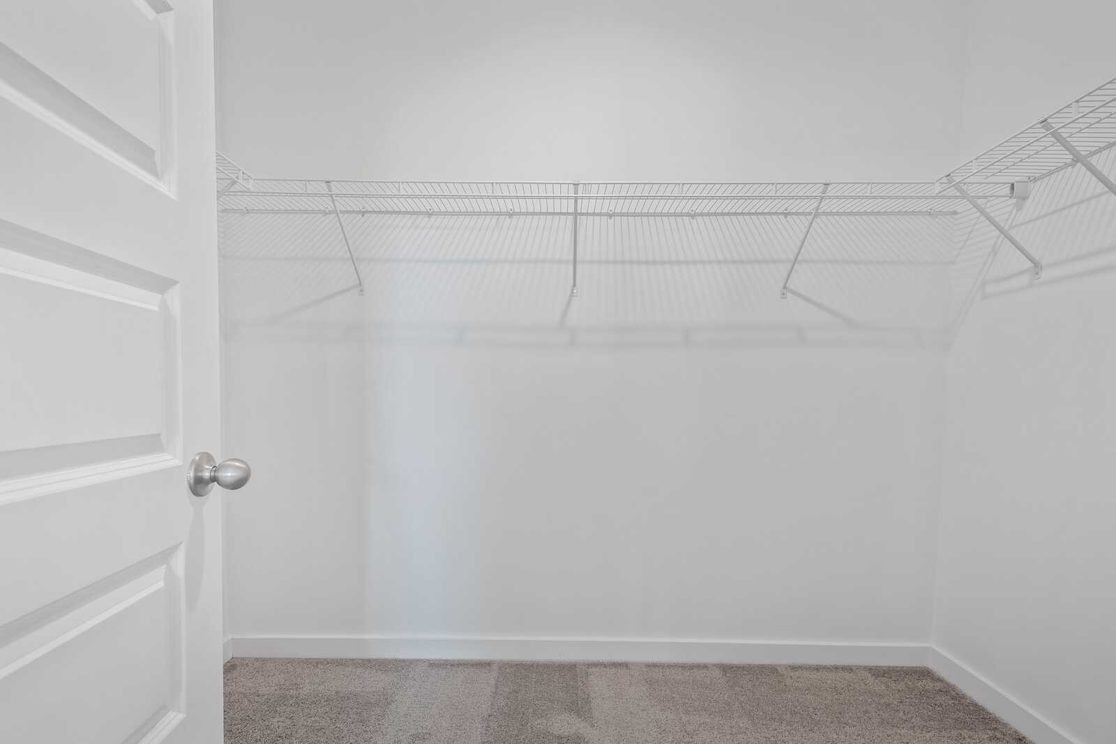 Spacious walk-in closet in The Asheville master suite with open white door, wire shelving, and beige carpet floor